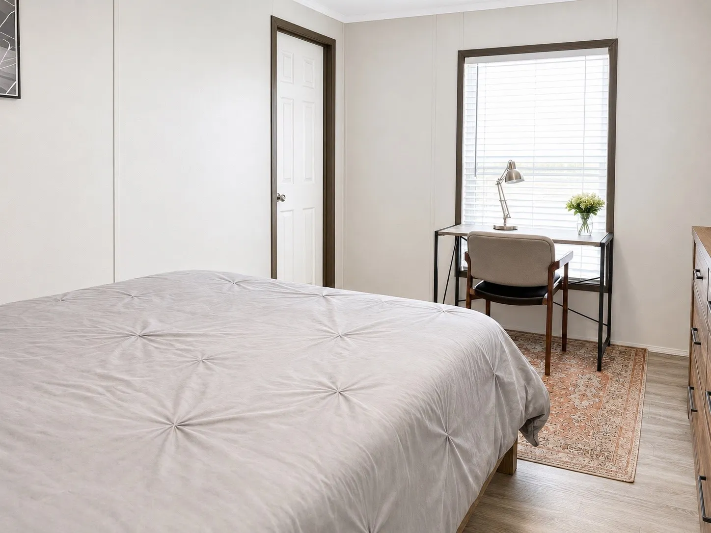 Neutral-toned room with wood-finish flooring, a white paneled door with dark trim, and a window featuring blinds