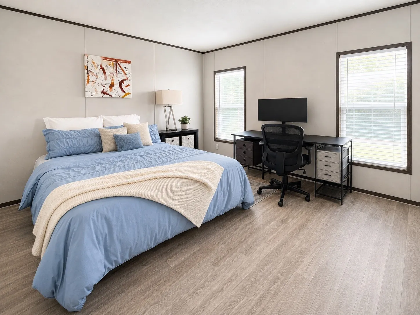 Spacious room featuring light wood-finish flooring, two large windows with blinds, and white panel walls with dark trim