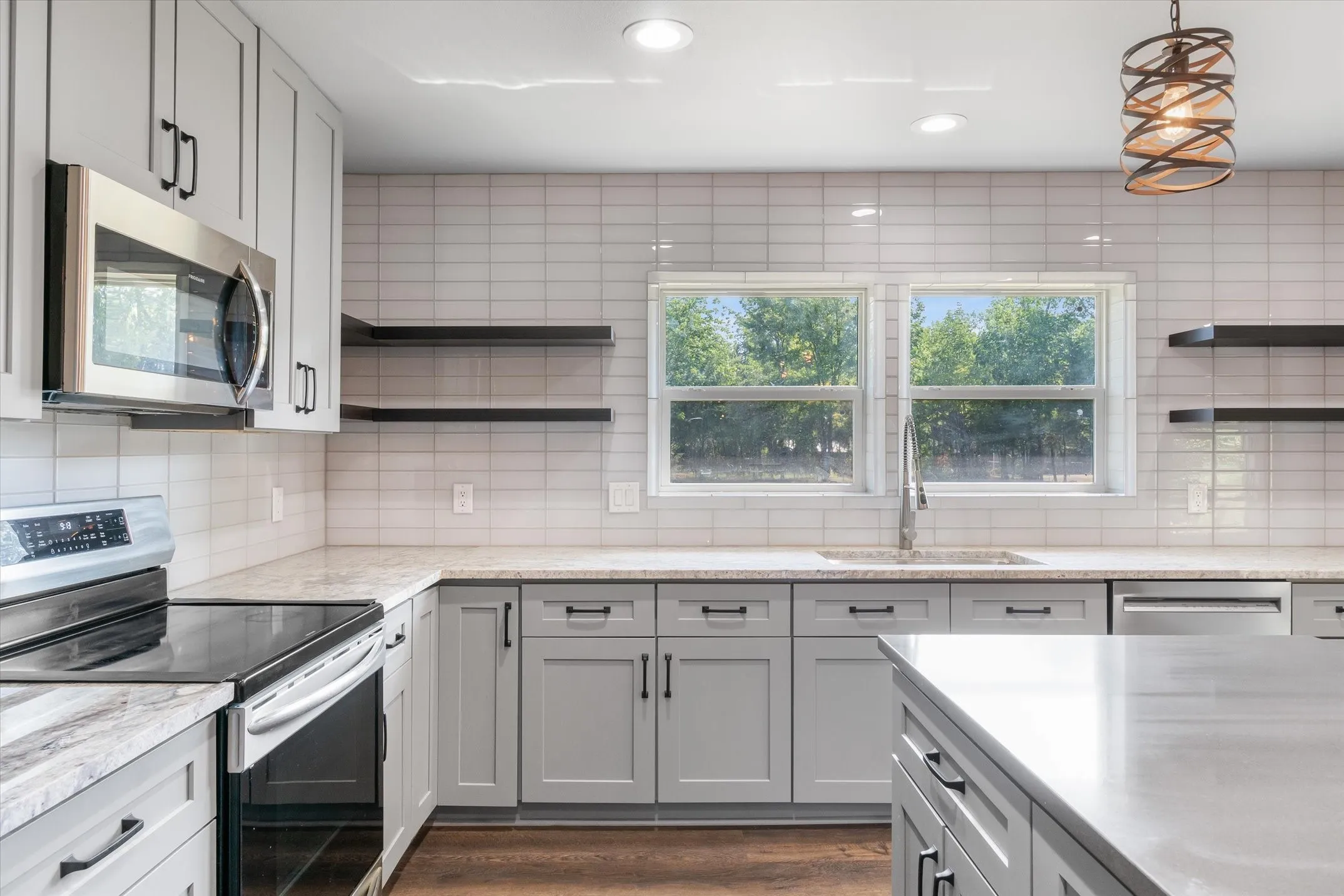 Kitchen featuring a subway tile backsplash, light grey cabinetry, stainless steel appliances, and wood-finish flooring