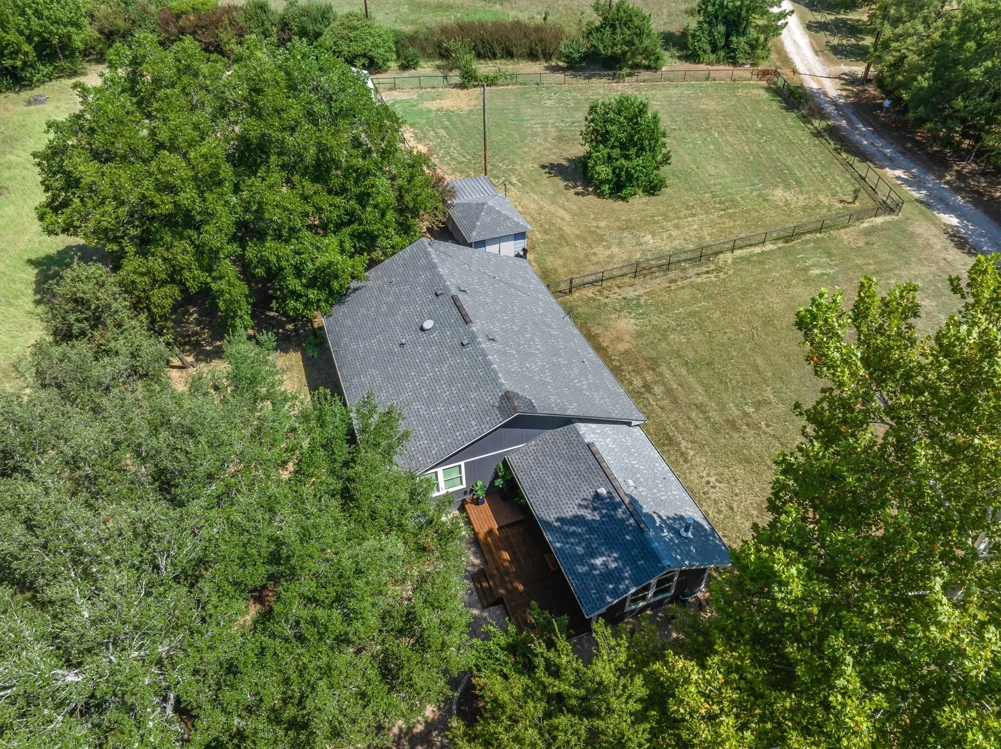 Aerial perspective of a property featuring a dark-toned residential structure with a gray shingle roof, accompanied by an outbuilding
