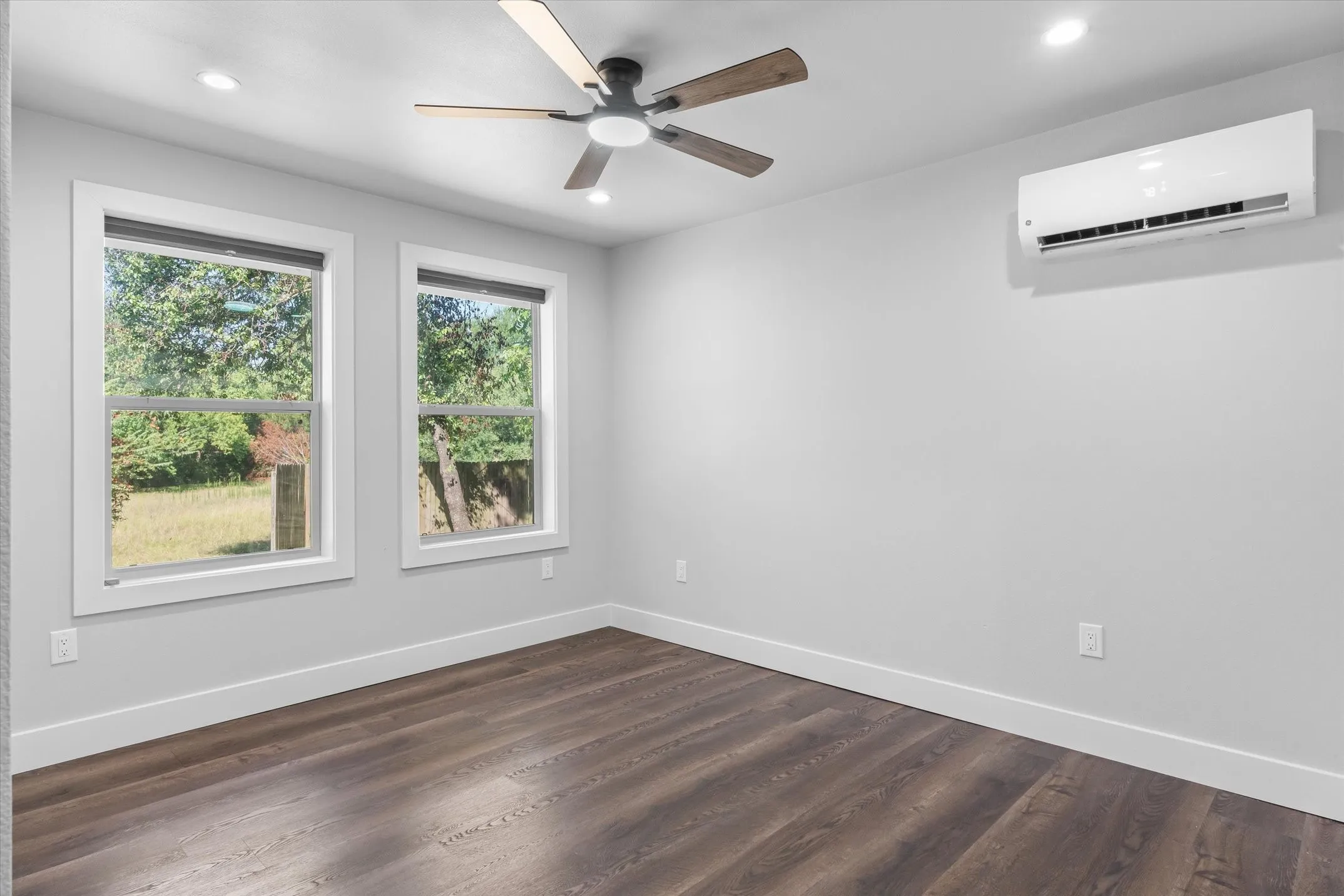 Room featuring wood-finish flooring, two large windows, a ceiling fan with integrated lighting, recessed lighting, and a wall-mounted air conditioning unit