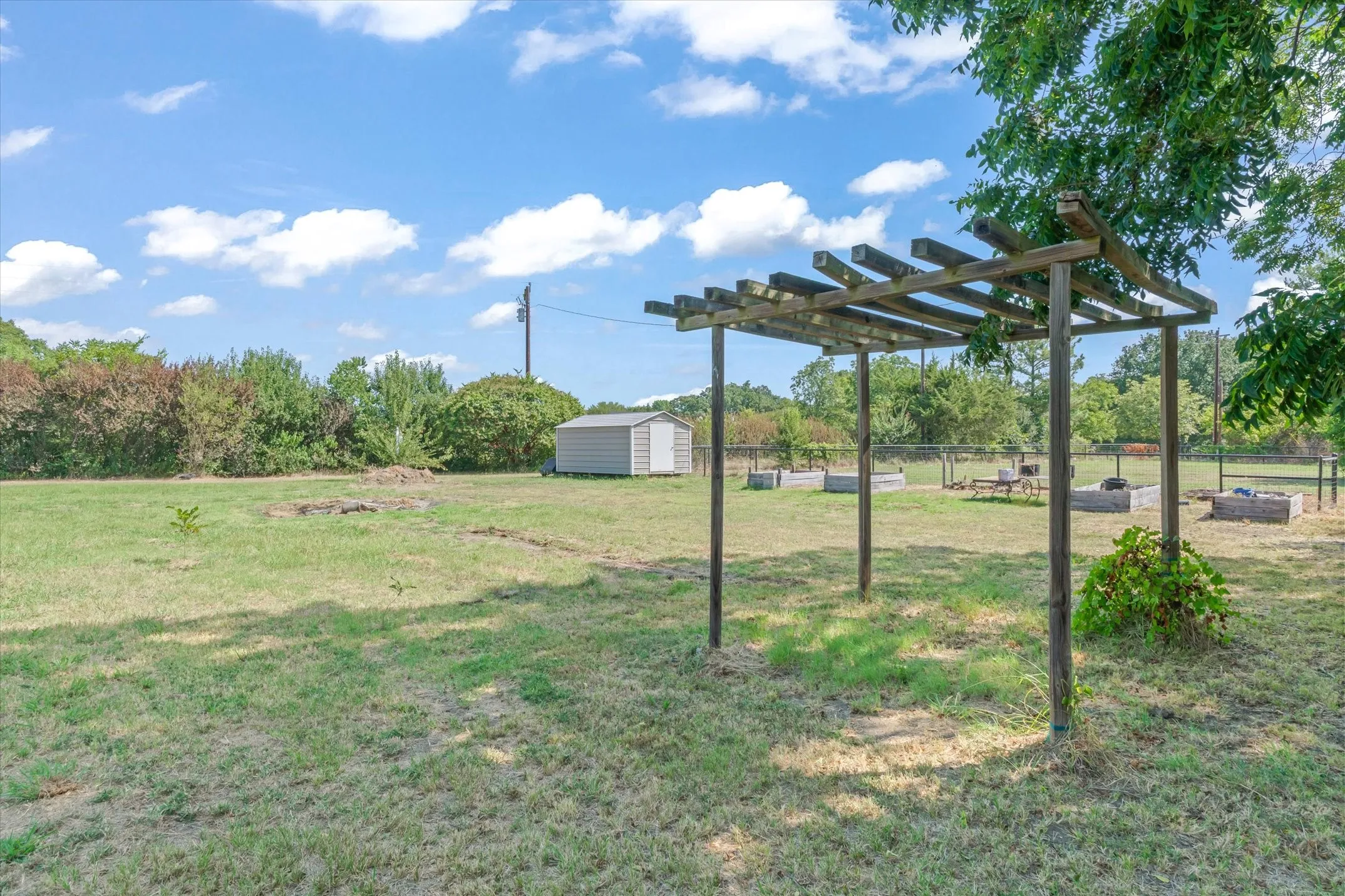 Expansive outdoor space featuring a wooden pergola, multiple raised garden beds, a storage shed, and mature trees