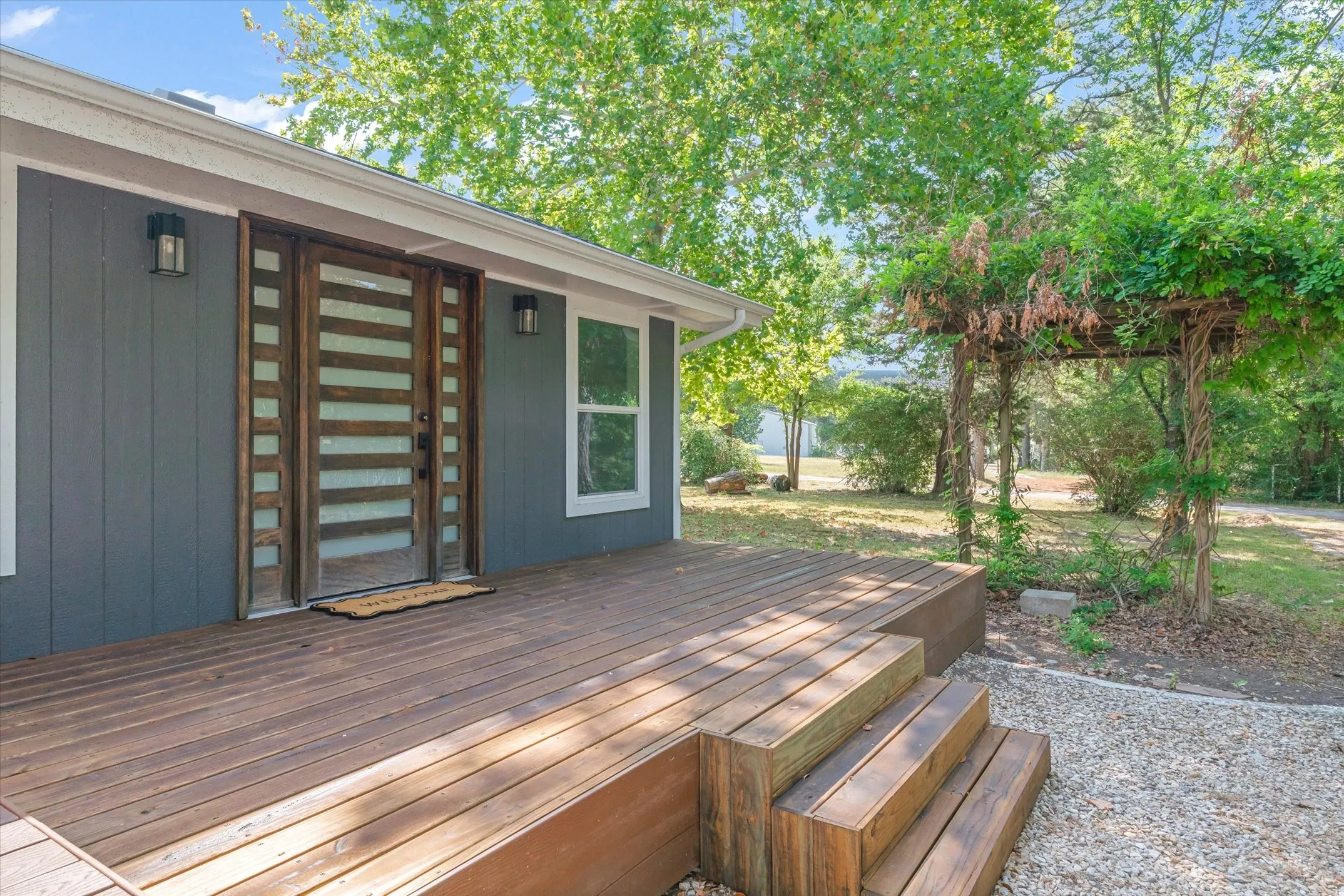 Expansive wood deck with multi-level steps and a modern wood entry door featuring frosted glass panels