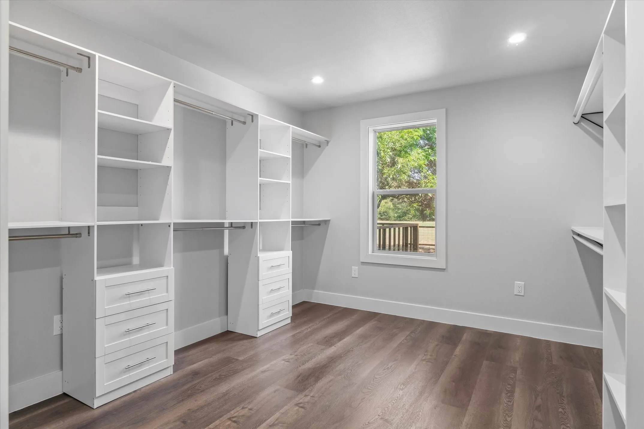 Spacious closet featuring extensive built-in white cabinetry, multiple hanging rods, integrated drawers with brushed nickel hardware, recessed lighting, and wood-finish flooring