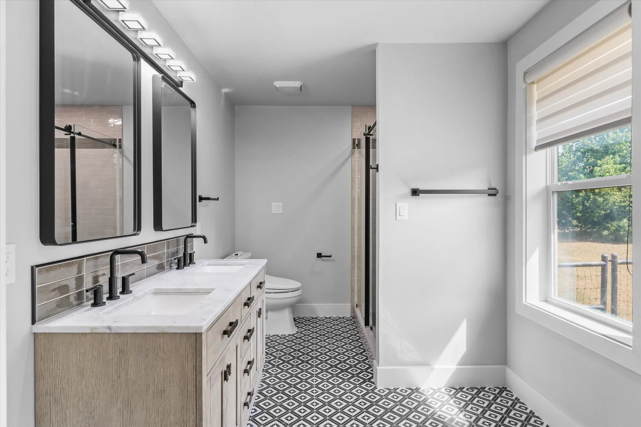 Bathroom featuring a dual vanity with a light wood-finish cabinet and white countertop, black framed mirrors, and black hardware
