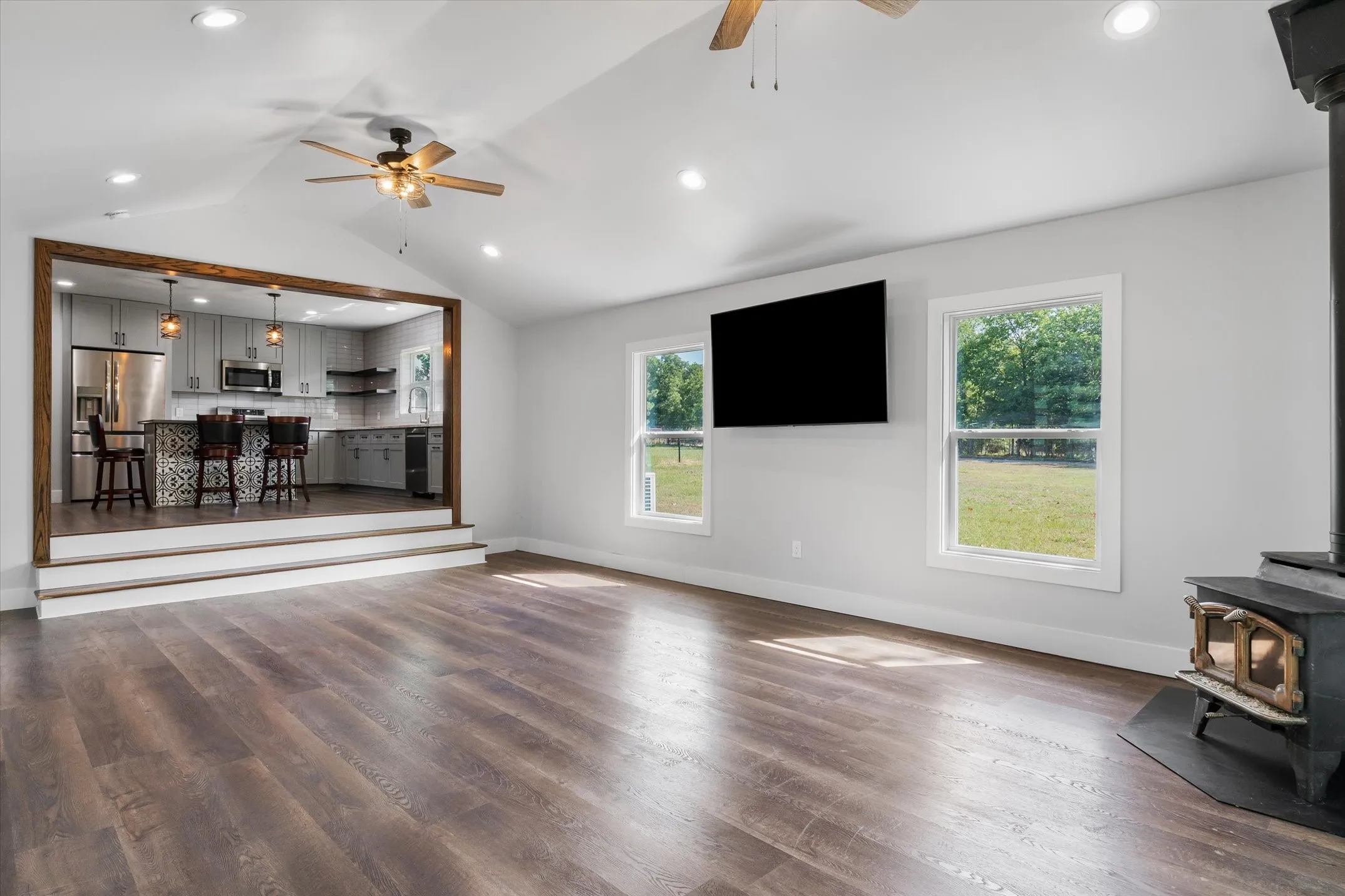 Vaulted ceiling living area featuring wood-finish flooring, recessed lighting, and a wood-burning stove