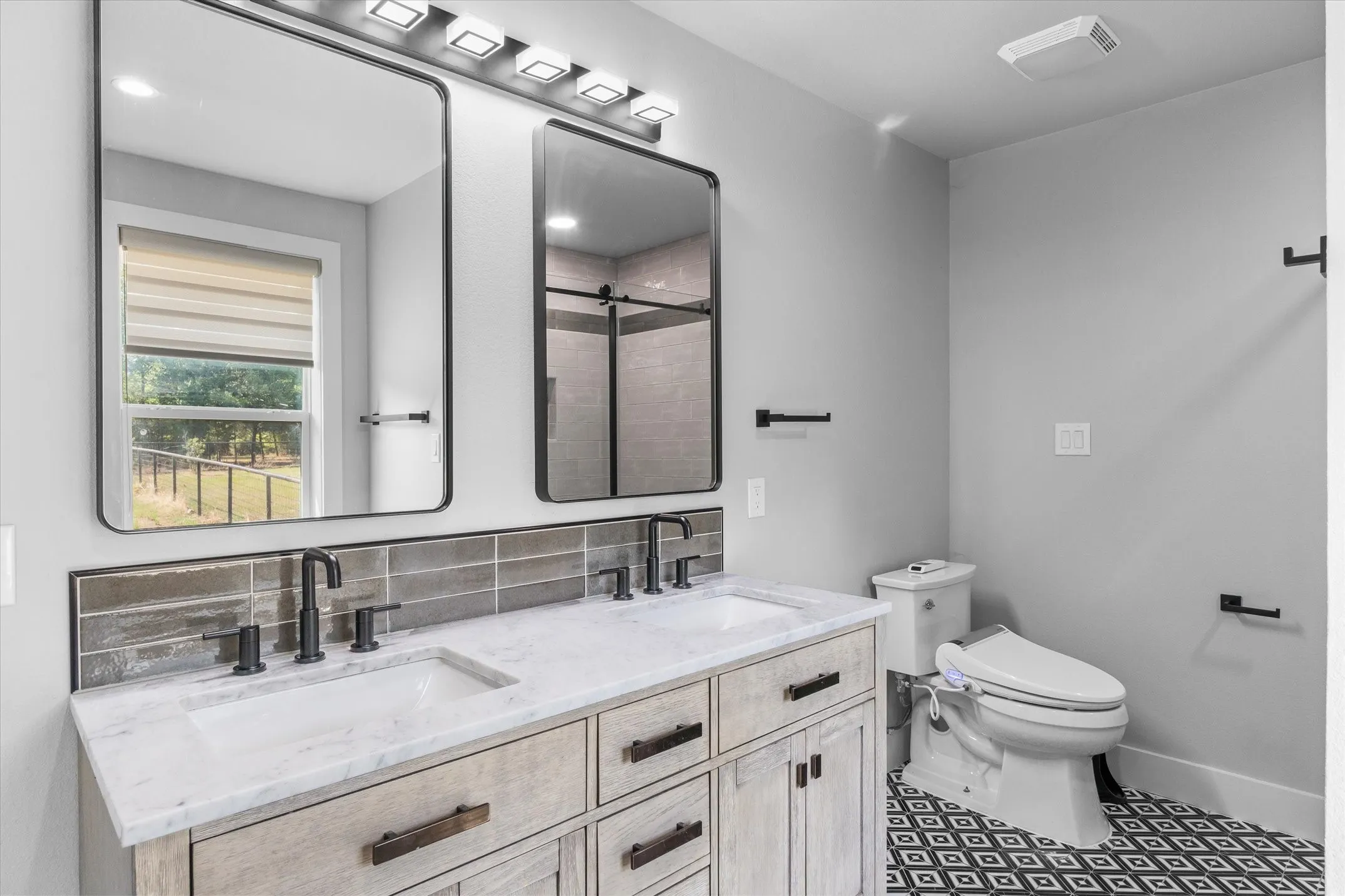 Dual vanity with integrated sinks, a gray subway tile backsplash, and matte black fixtures