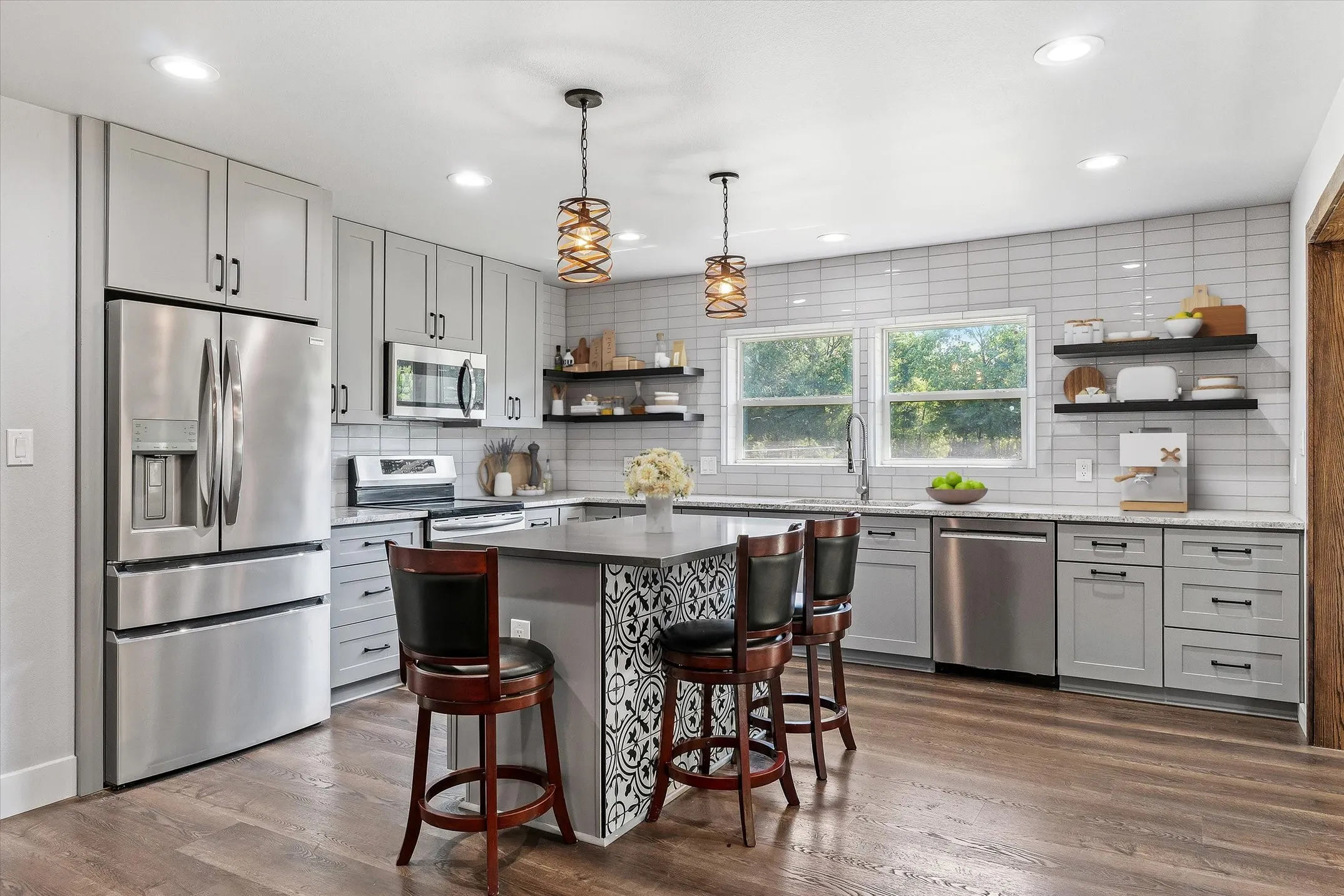 Digitally enhanced. Contemporary kitchen featuring grey cabinetry, stainless steel appliances, wood-finish flooring, white subway tile backsplash, and an island with seating