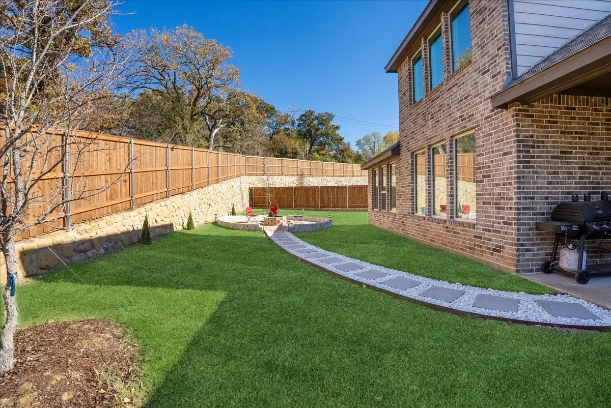 Spacious rear yard featuring an expansive lawn, a stone retaining wall, and a wood privacy fence