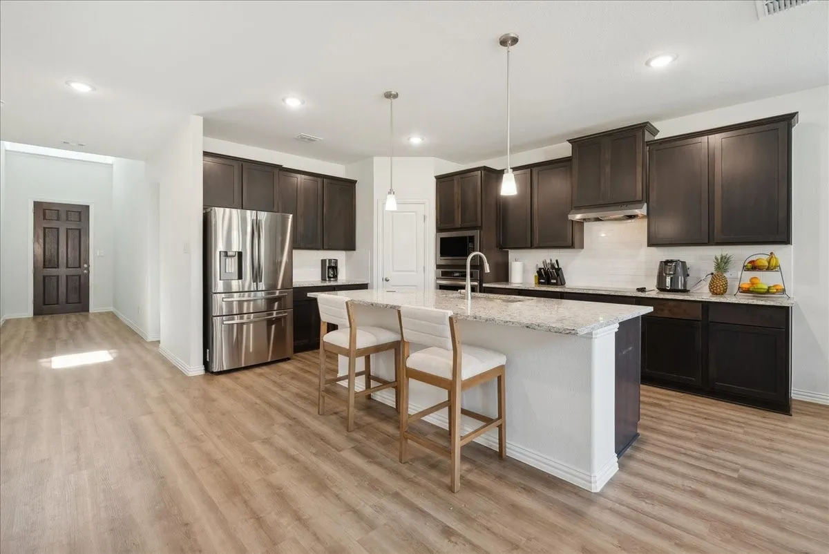 Gourmet kitchen featuring dark wood cabinetry, stainless steel appliances, a center island with bar seating, pendant lighting, and wood-finish flooring