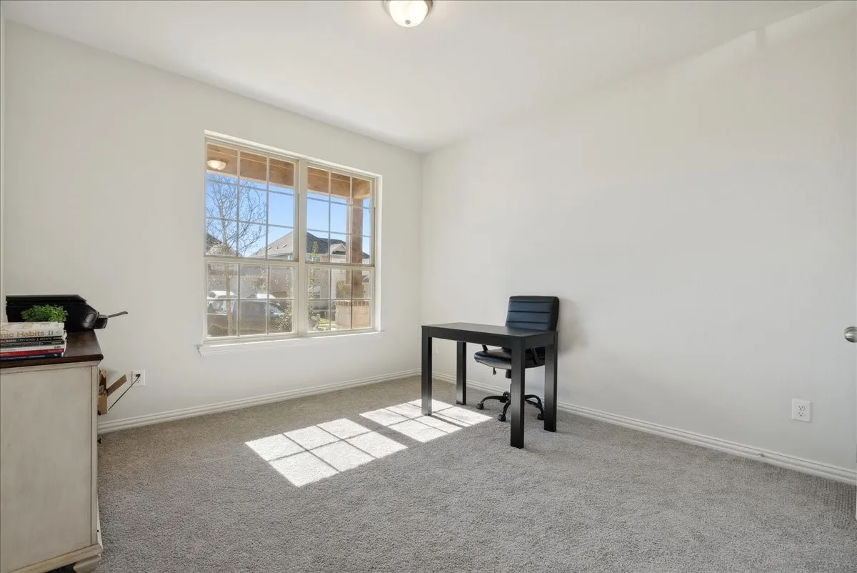 Spacious room featuring a large window with white framing, soft gray carpeting, white baseboards, and a semi-flush mount ceiling light fixture