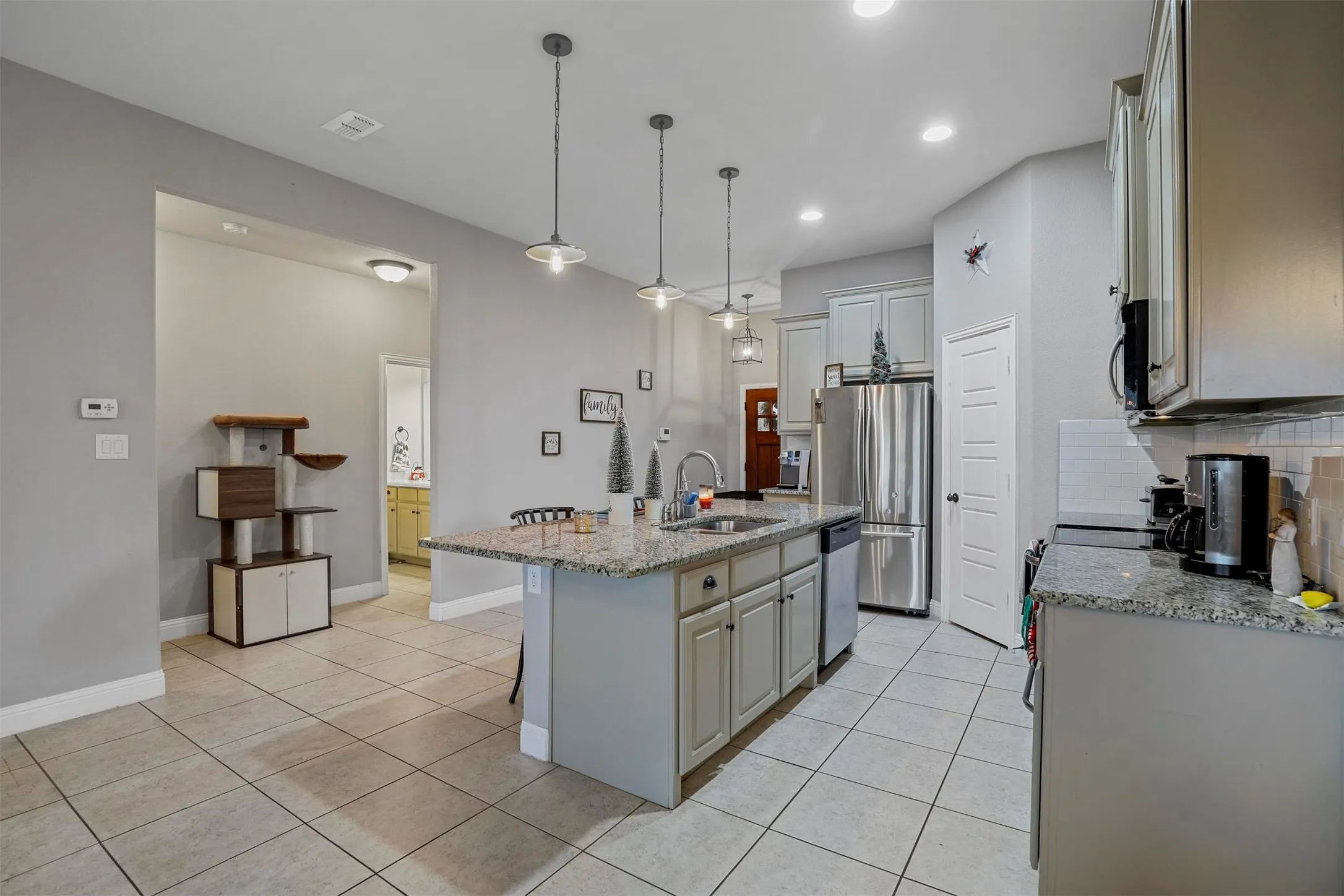Kitchen featuring a central island with integrated sink, granite countertops, and light-toned cabinetry