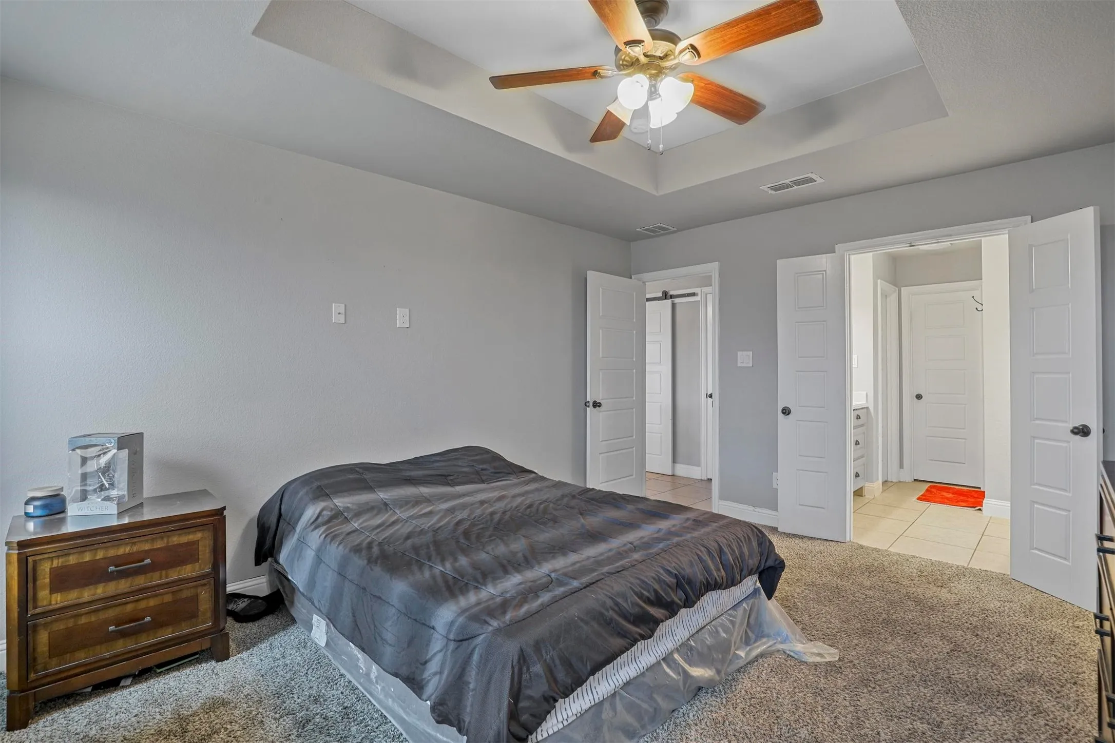 Bedroom featuring a tray ceiling with a ceiling fan, light gray painted walls, and carpet flooring