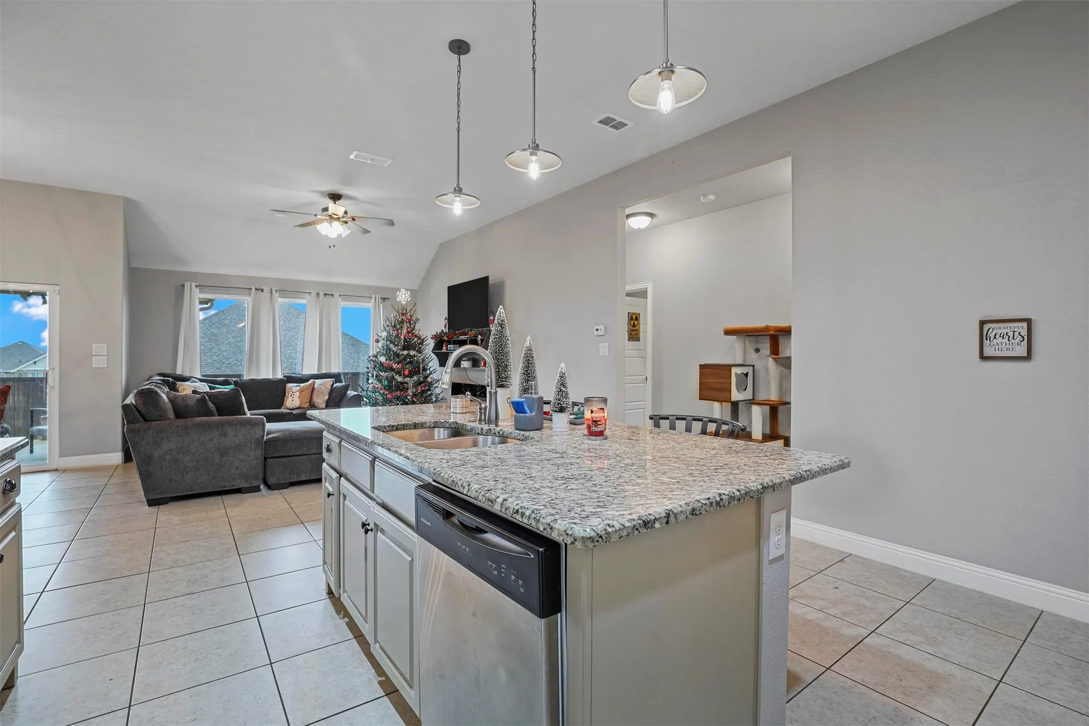 Open-concept living area featuring a kitchen island with integrated sink, pendant lighting, and a dishwasher
