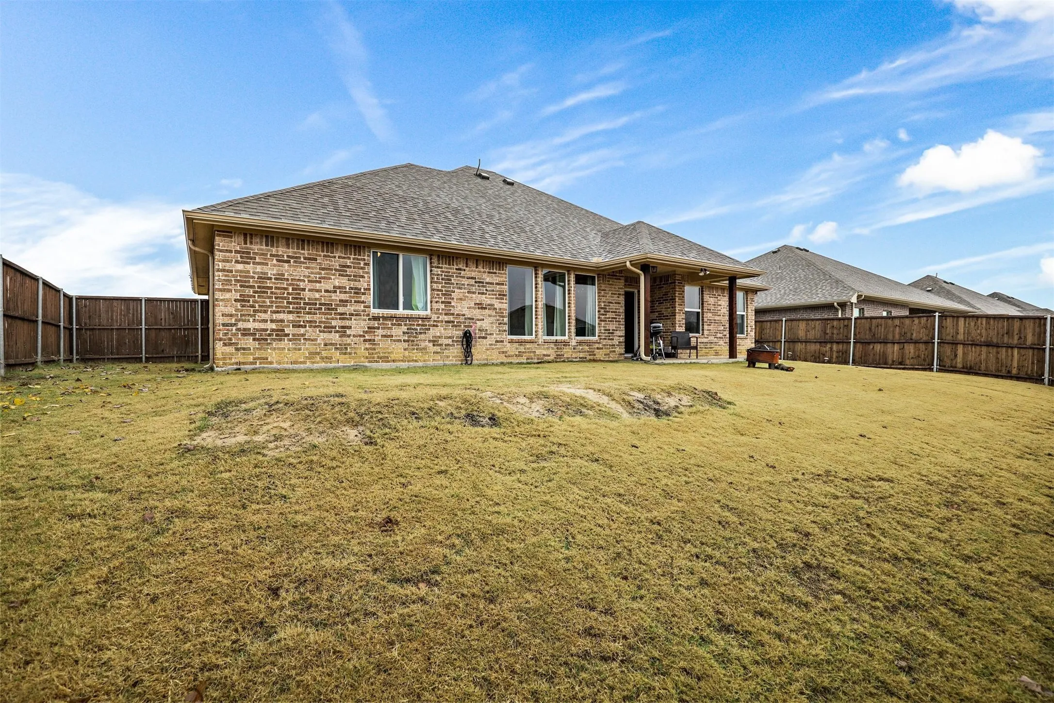 Expansive backyard featuring a brick exterior, multiple windows, a covered patio, and wood privacy fencing