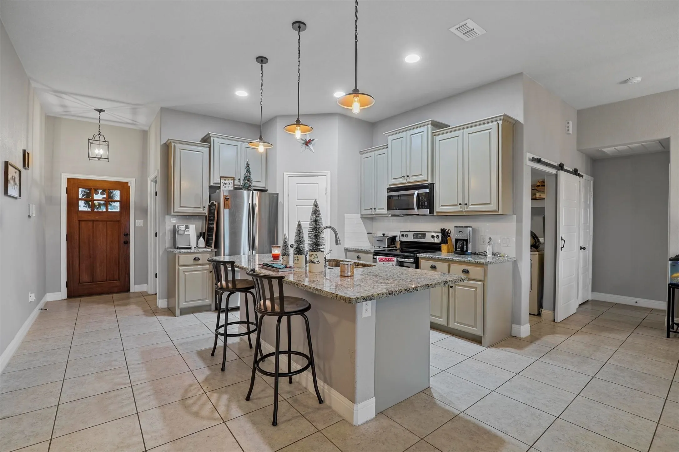 Open-concept kitchen featuring an island with granite-style countertop, stainless steel appliances, pendant lighting, and tile flooring