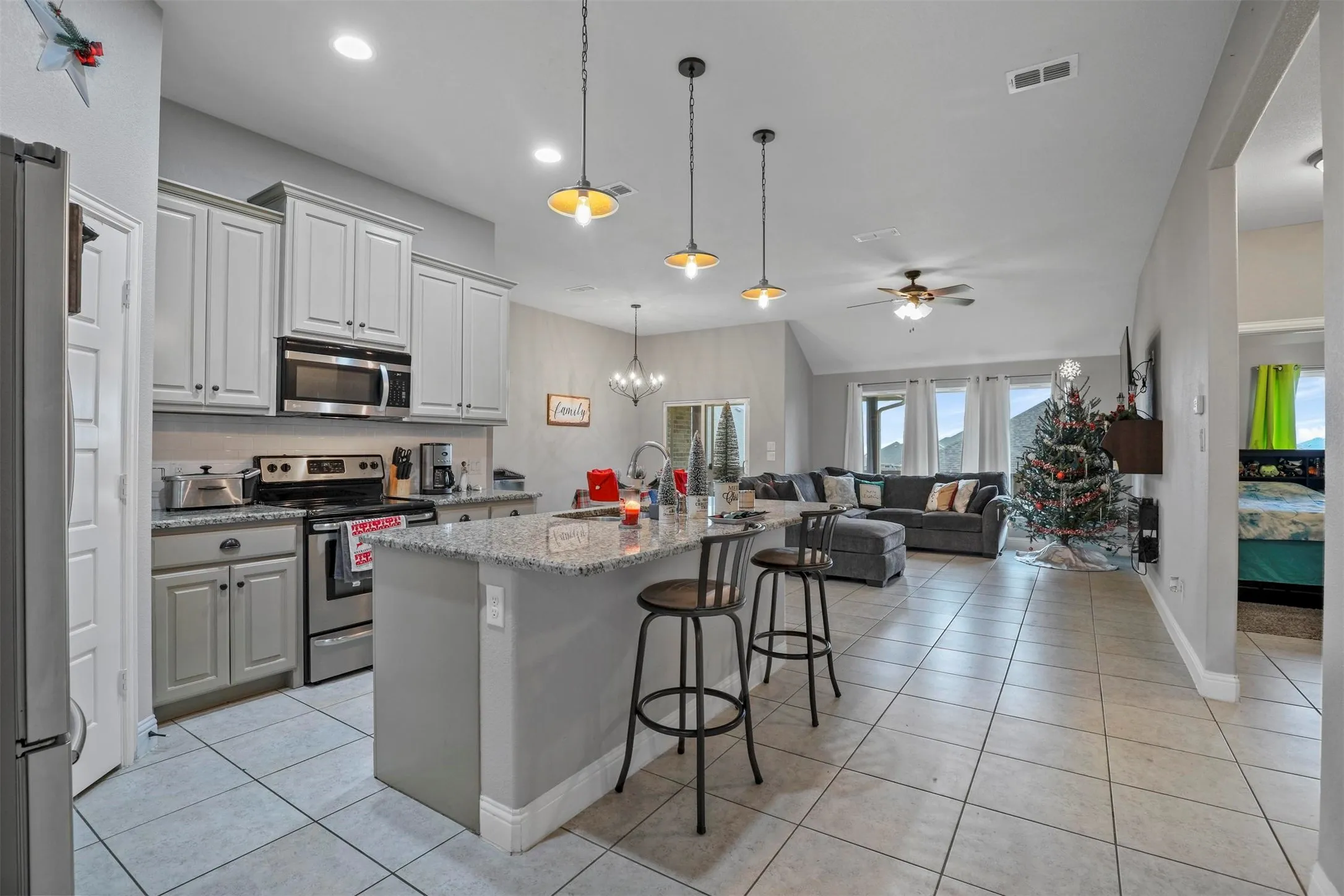 Open-concept kitchen featuring light-toned cabinetry, granite-style countertops, stainless steel appliances, and a central island with pendant lighting