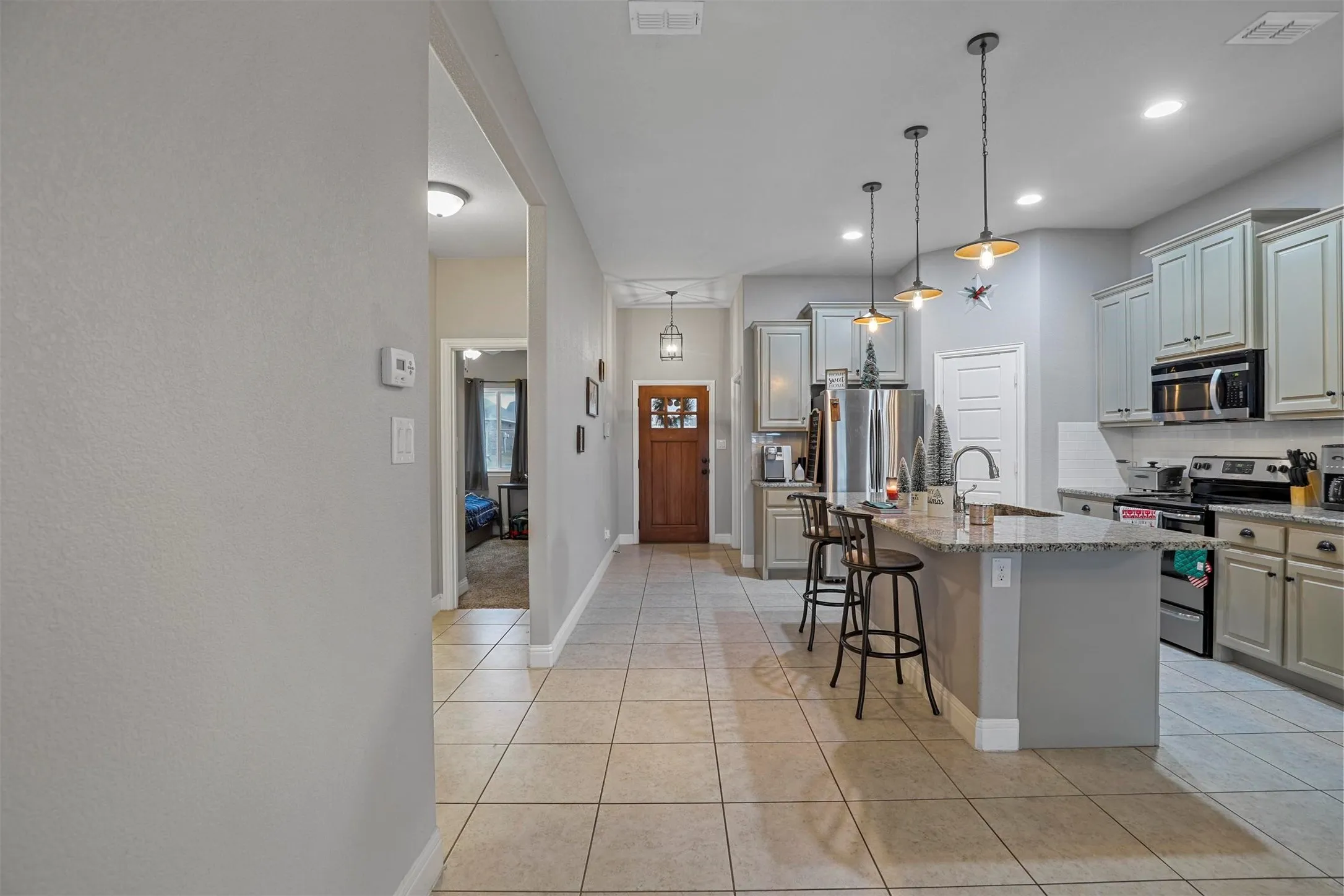 Open-concept kitchen featuring light-toned cabinetry, stainless steel appliances, a center island with bar seating, pendant lighting, and tile flooring
