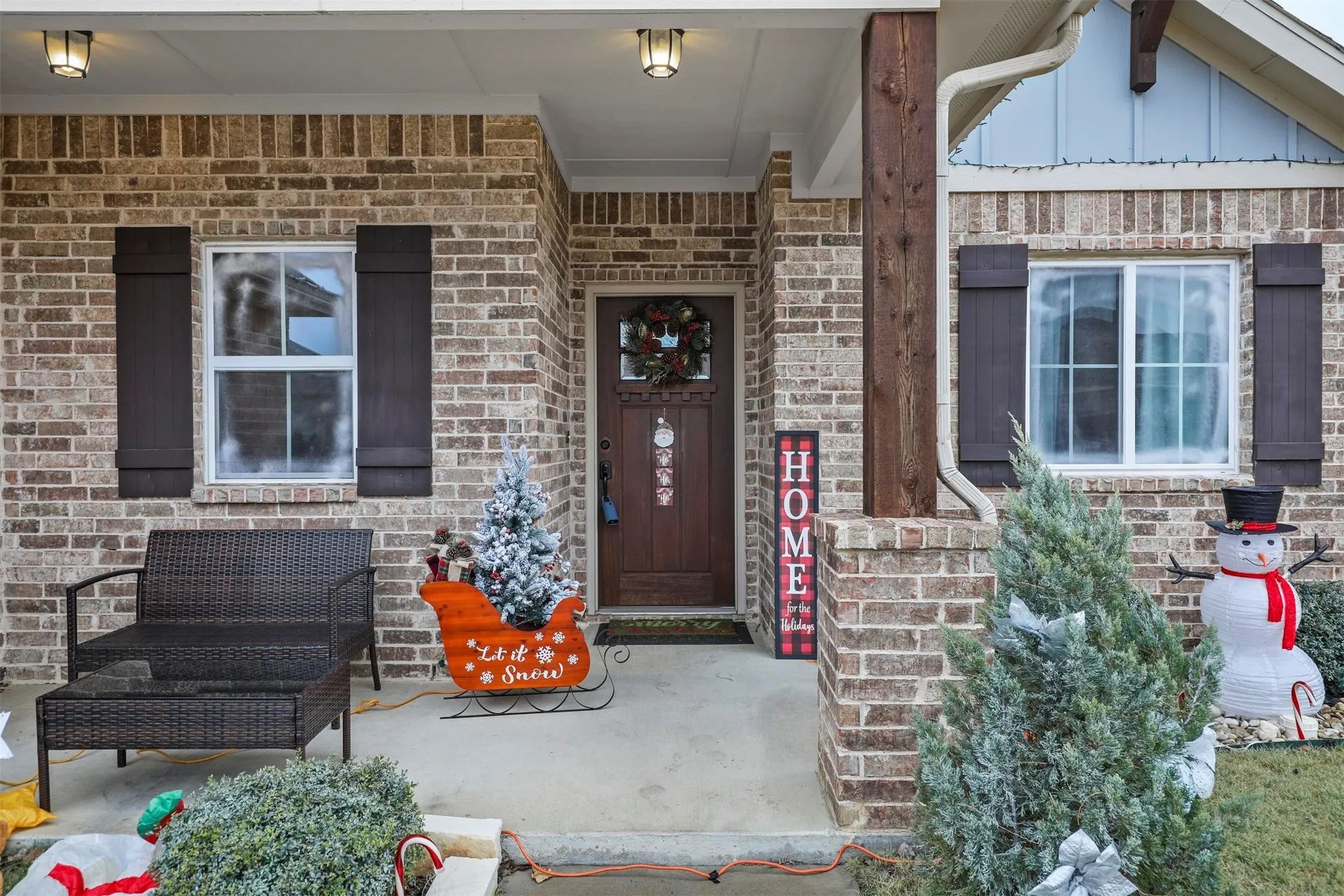 Brick exterior featuring a covered porch, dark wood-finish shutters, and a prominent wood-clad column