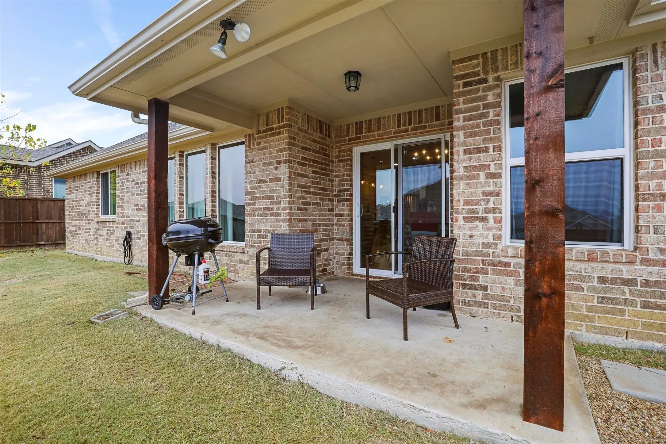 Covered concrete patio featuring a brick exterior with white trim windows and a glass sliding door