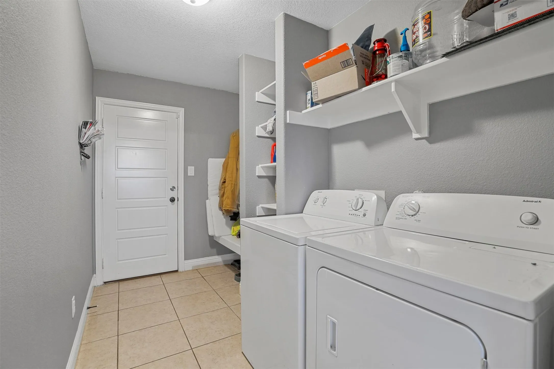 Laundry area featuring tile flooring, white shelving, a built-in bench, and a paneled door