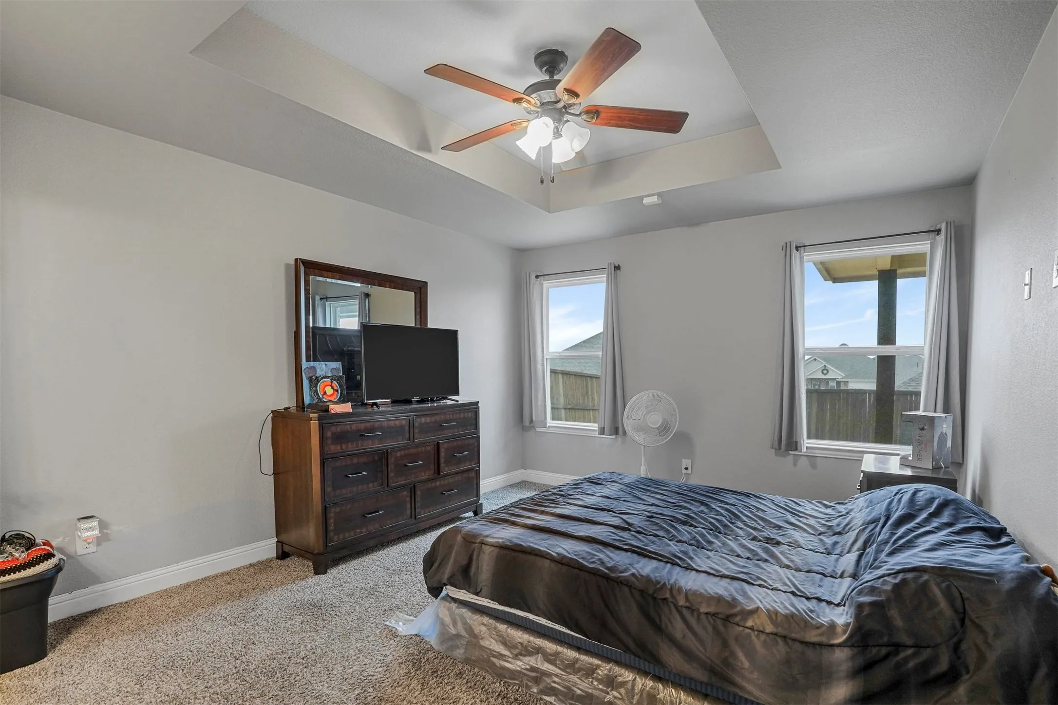 Spacious room featuring a tray ceiling with a built-in ceiling fan, light gray wall paint, and plush carpet flooring