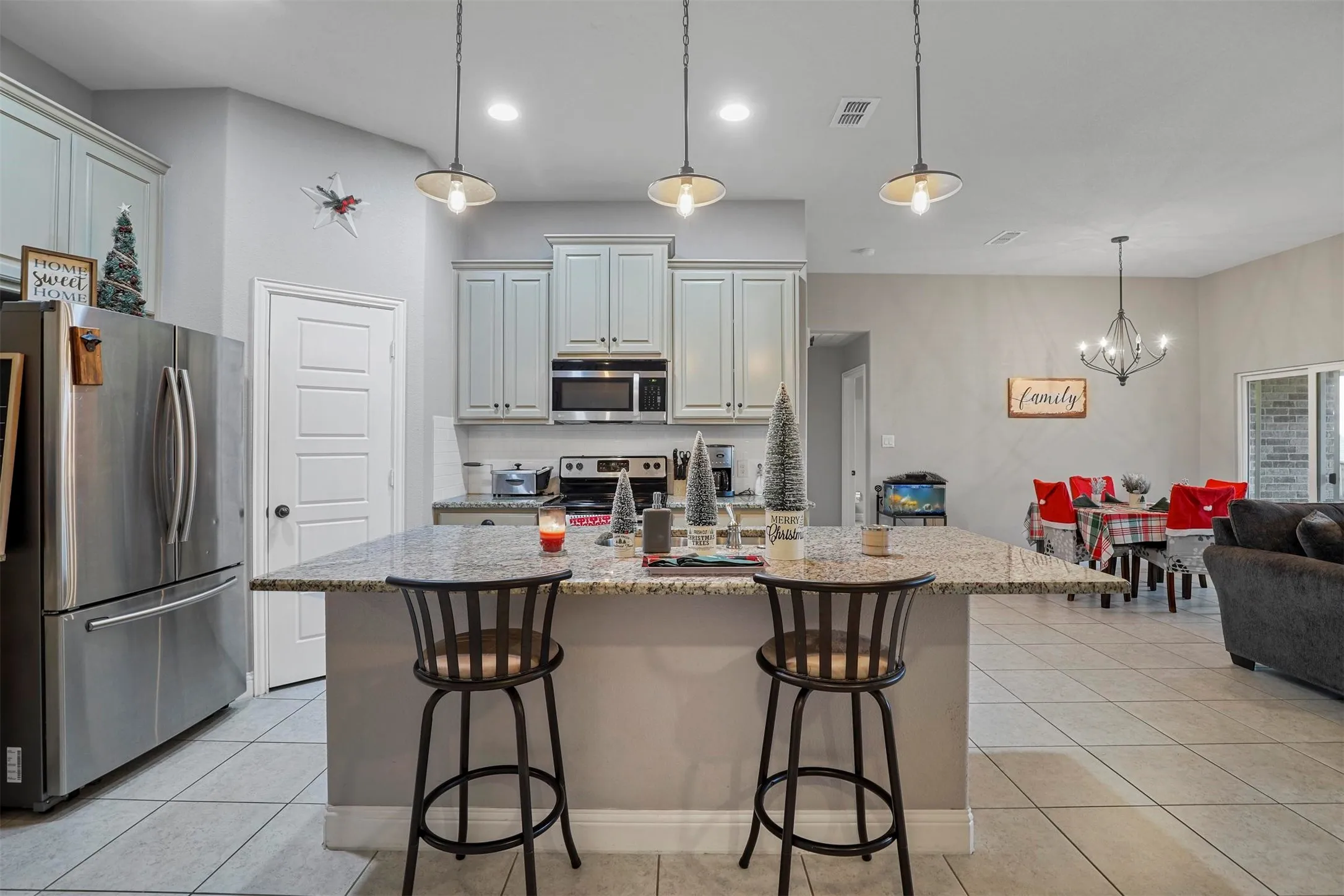 Kitchen featuring a granite-finish island with pendant lighting, stainless steel appliances, light-toned cabinetry, and tile flooring