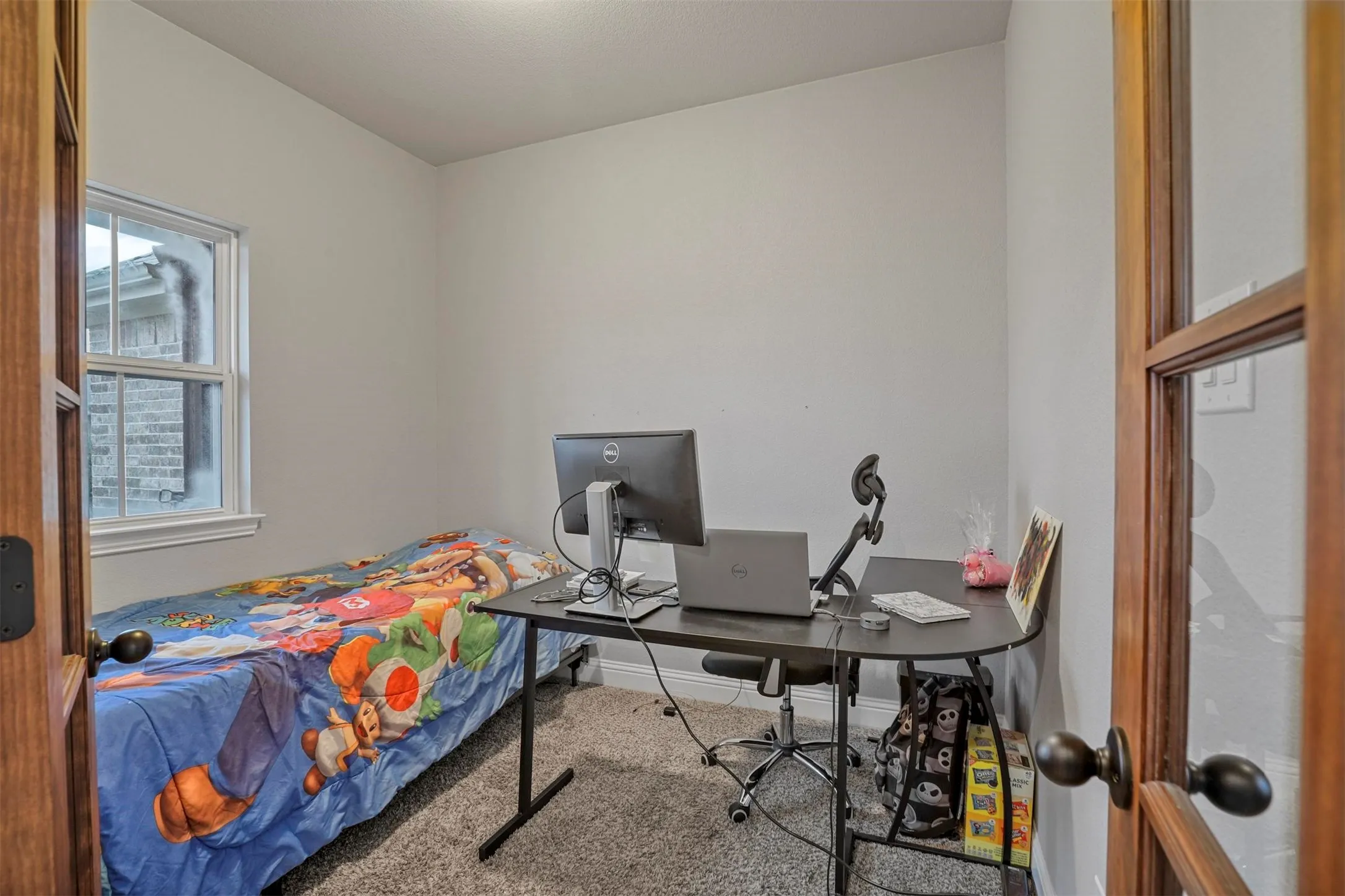 French doors with glass panels open to a versatile room featuring light gray walls, plush gray carpet, and a white-framed window