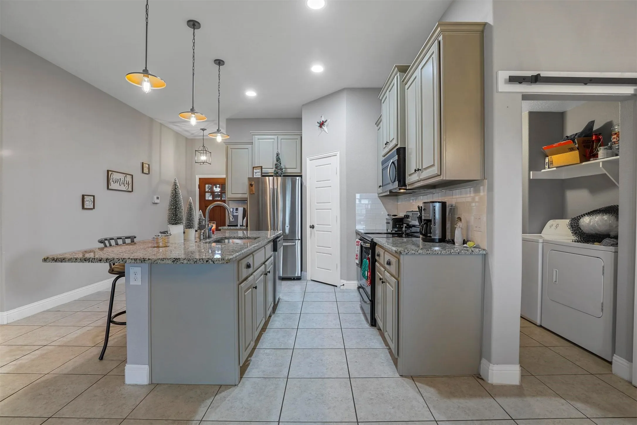 Kitchen featuring an island with stone countertops, pendant lighting, stainless steel appliances, and tile flooring