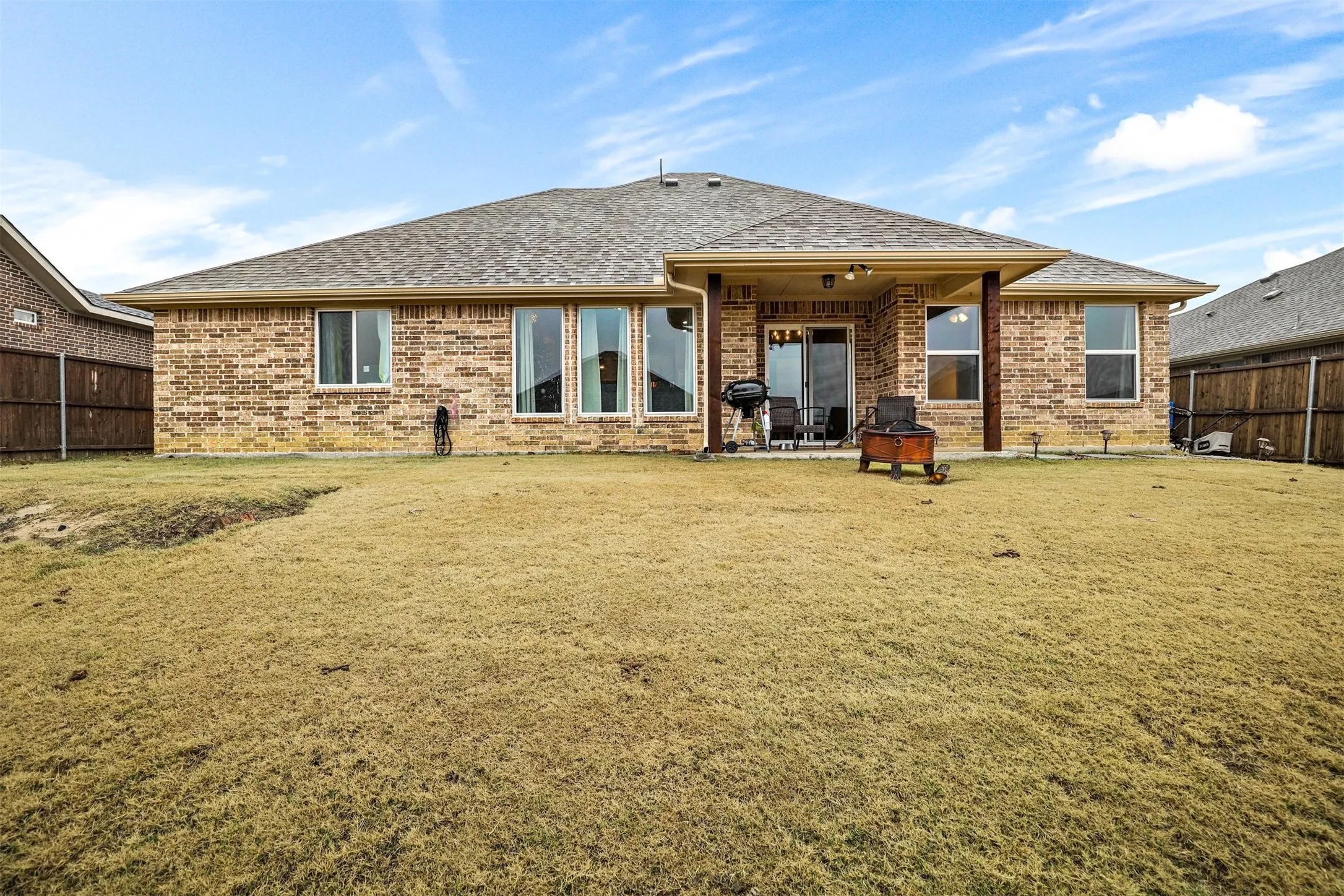 Rear exterior featuring a covered patio, brick facade, and a fenced perimeter