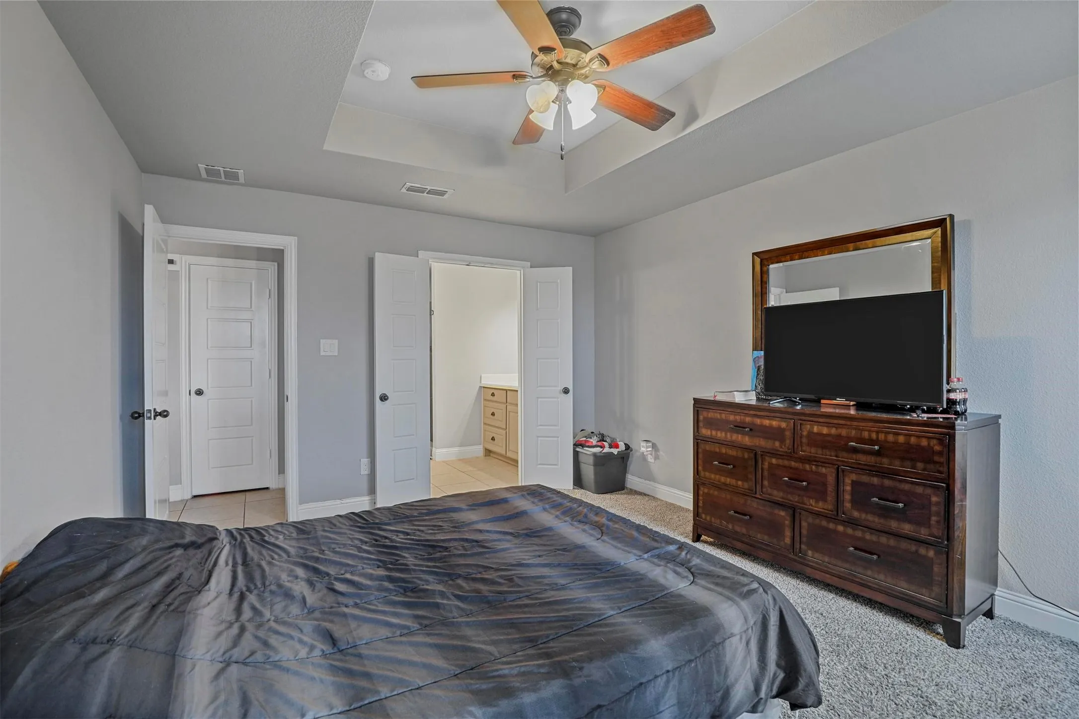 Recessed tray ceiling with ceiling fan, light gray wall paint, and double door entry