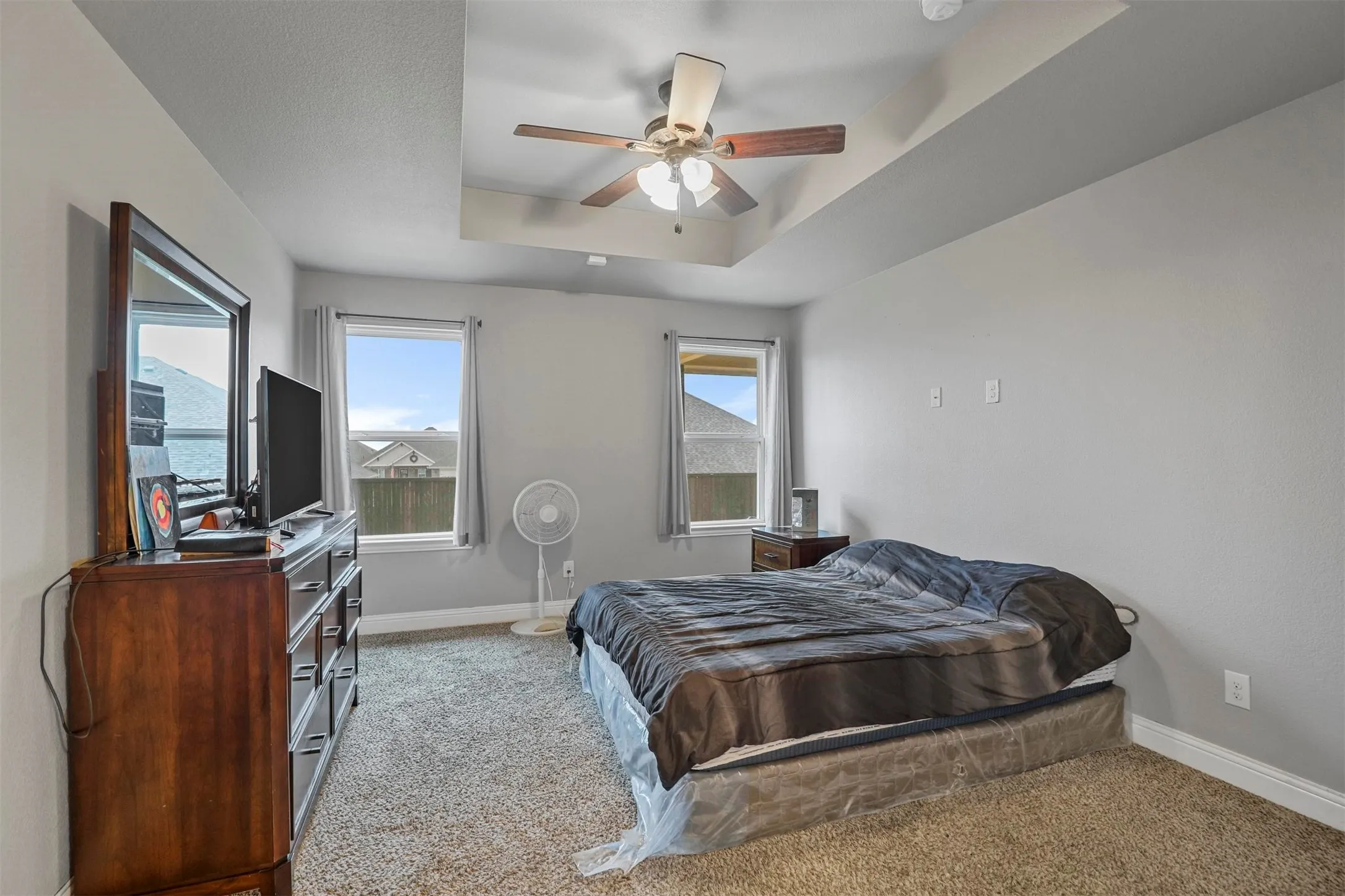 Spacious room featuring a tray ceiling with a ceiling fan, two windows with vertical blinds, light gray walls, and carpet flooring
