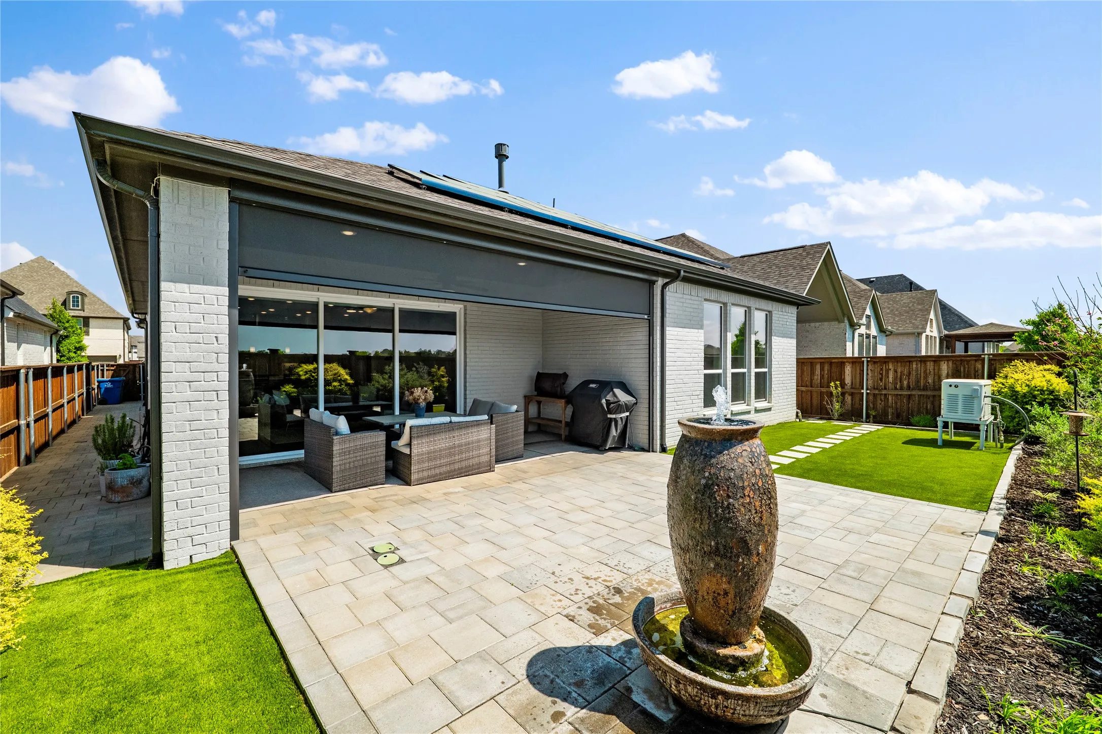 Rear view of property with a fenced backyard, a patio area, brick siding, an outdoor hangout area, and solar panels