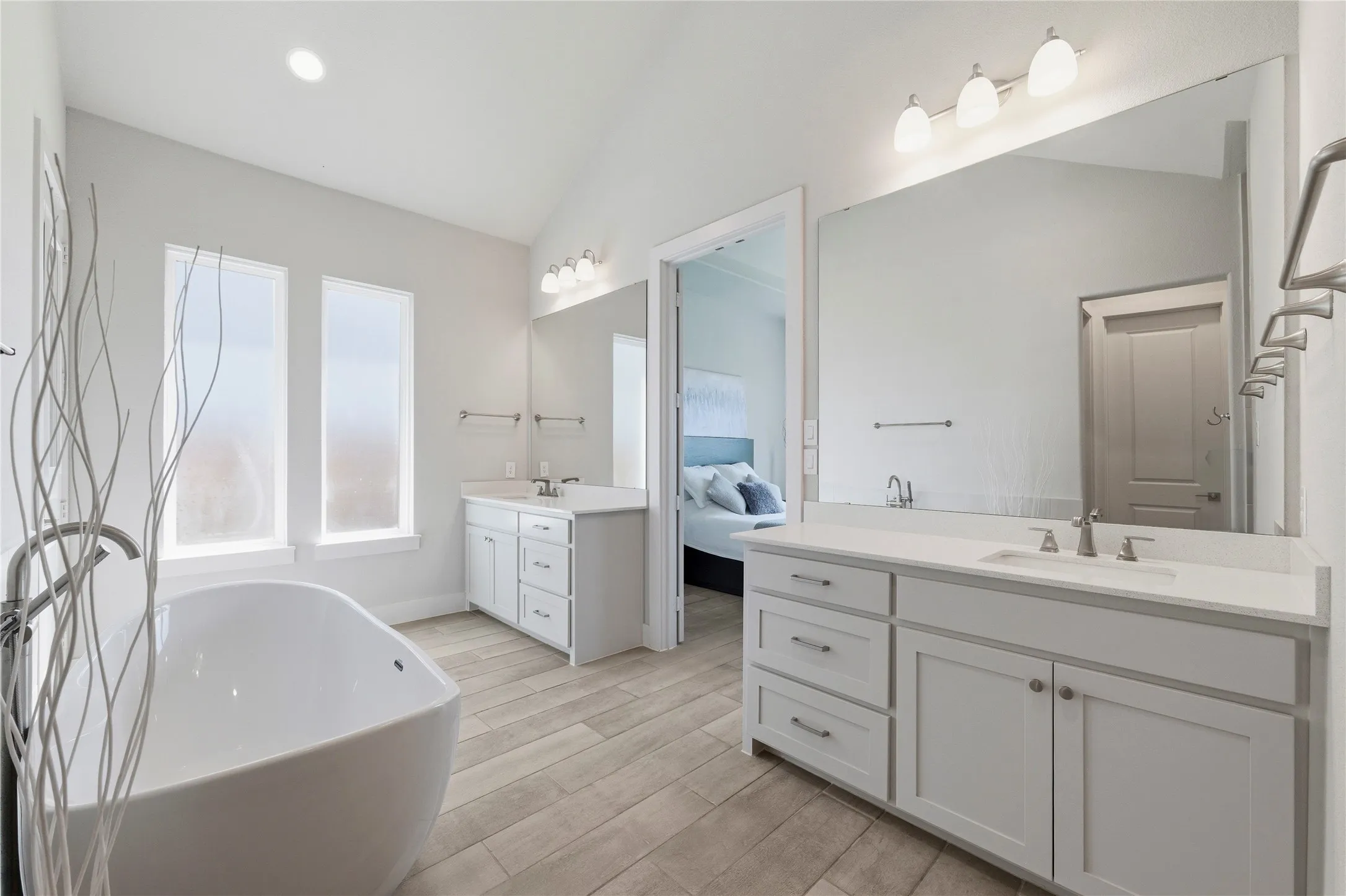 Ensuite bathroom with two vanities, lofted ceiling, wood tiled floors, a freestanding bath, and recessed lighting