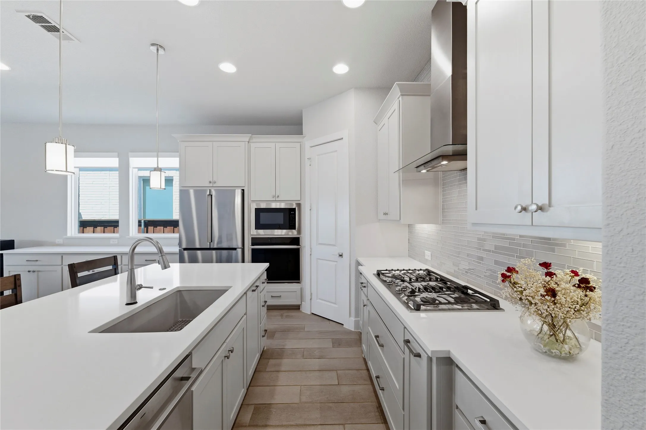Kitchen with white cabinets, decorative light fixtures, stainless steel appliances, light wood-type flooring, and light stone countertops