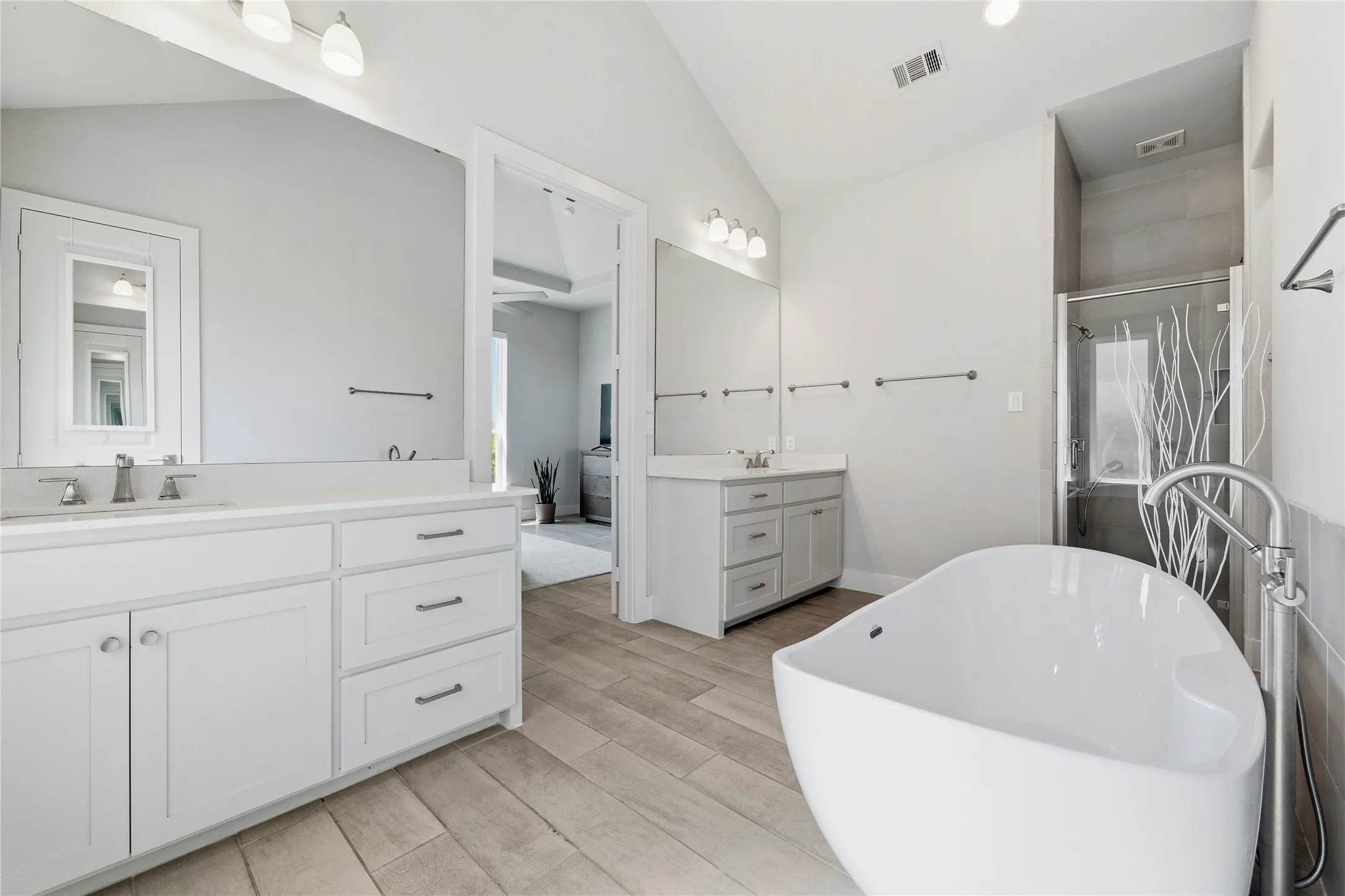 Ensuite bathroom featuring two vanities, a shower stall, light wood finished floors, lofted ceiling, and a freestanding bath