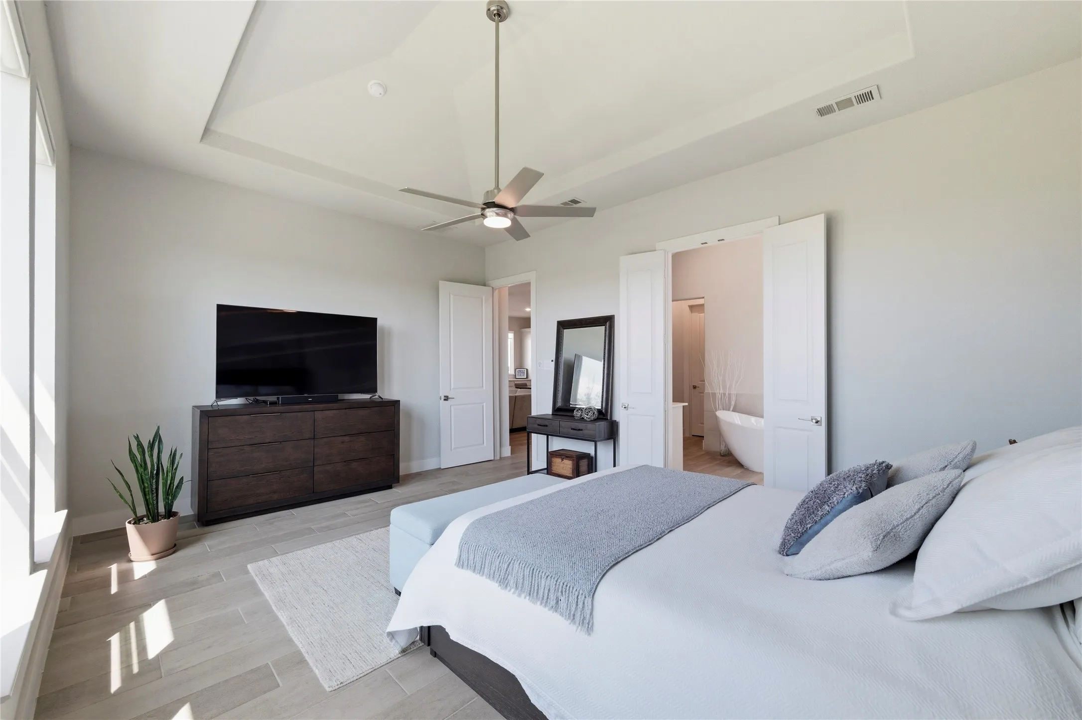 Bedroom with wood tiled floors, a raised ceiling, and ceiling fan