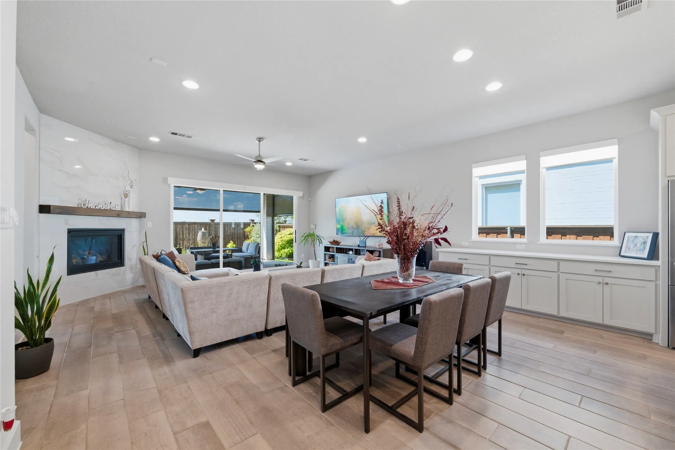 Dining space with light wood finished floors, a ceiling fan, a glass covered fireplace, and recessed lighting