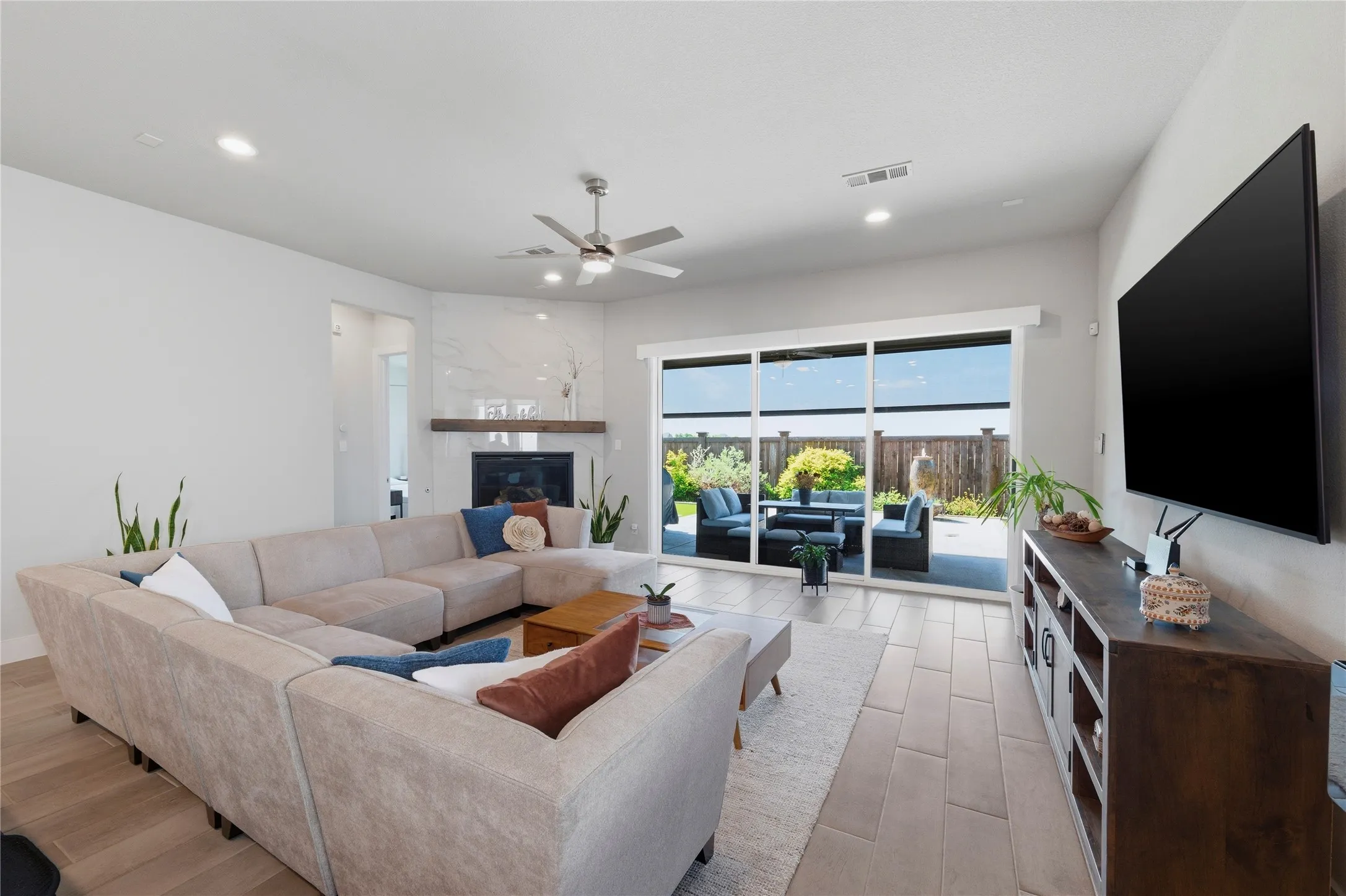 Living area with ceiling fan, a glass covered fireplace, light wood-style floors, and recessed lighting
