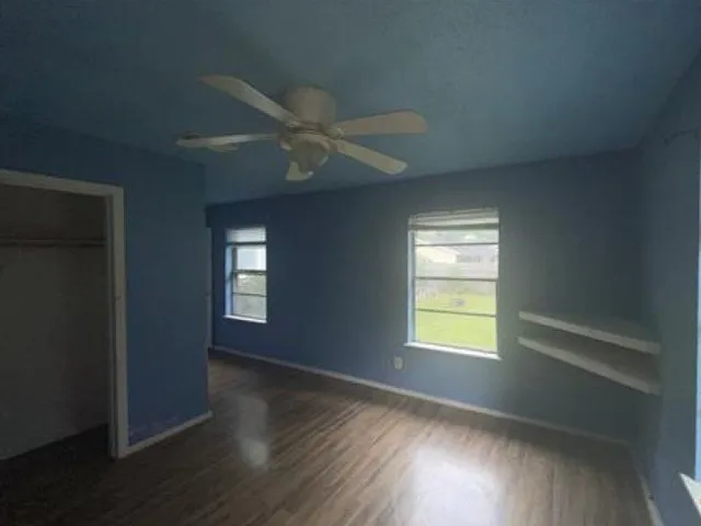 Room featuring wood-finish flooring, a ceiling fan with integrated lighting, and dual windows