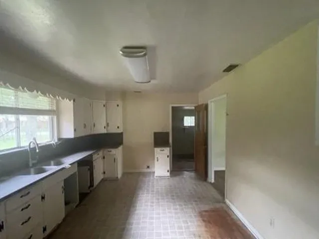 Kitchen with a double basin stainless steel sink, a modern gooseneck faucet, white cabinetry with dark hardware, and a tile-look flooring