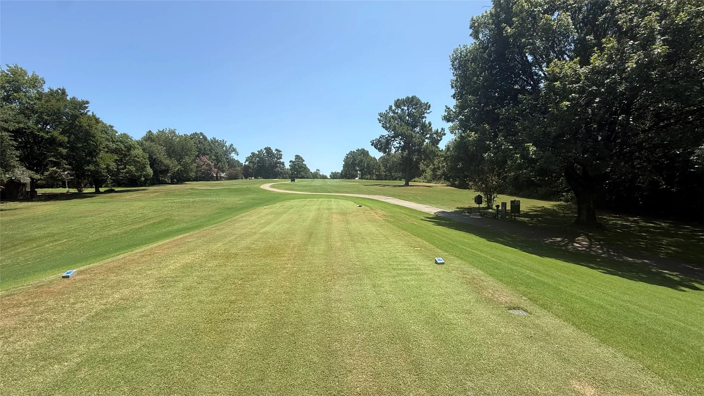 Expansive green space featuring a manicured lawn, established trees, and a visible golf course path