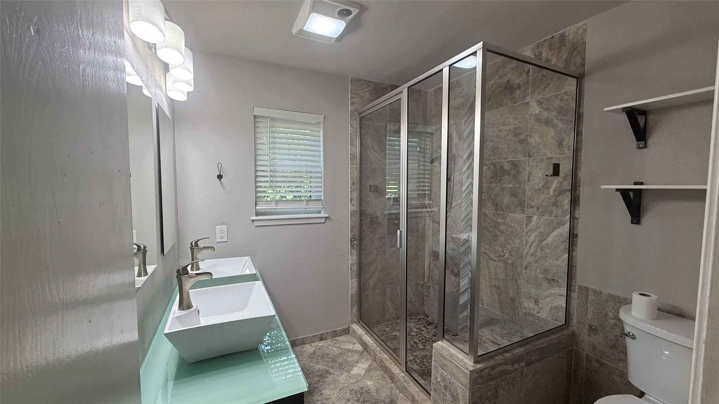 Bathroom featuring a dual vanity with vessel sinks, a glass-enclosed shower with stone tile, and built-in shelving