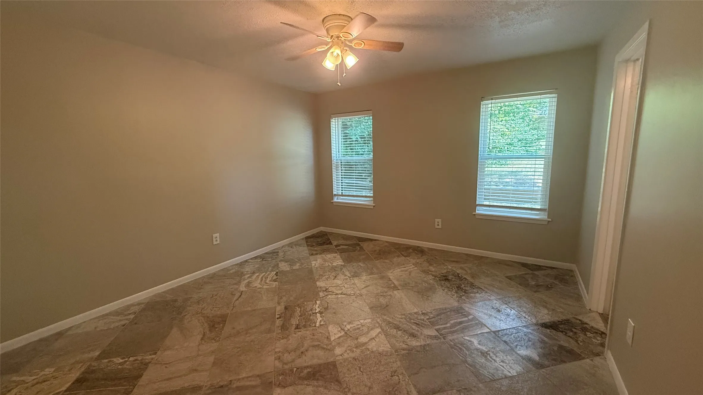 Spacious room featuring multi-tone tile flooring, neutral wall paint, and two windows with blinds