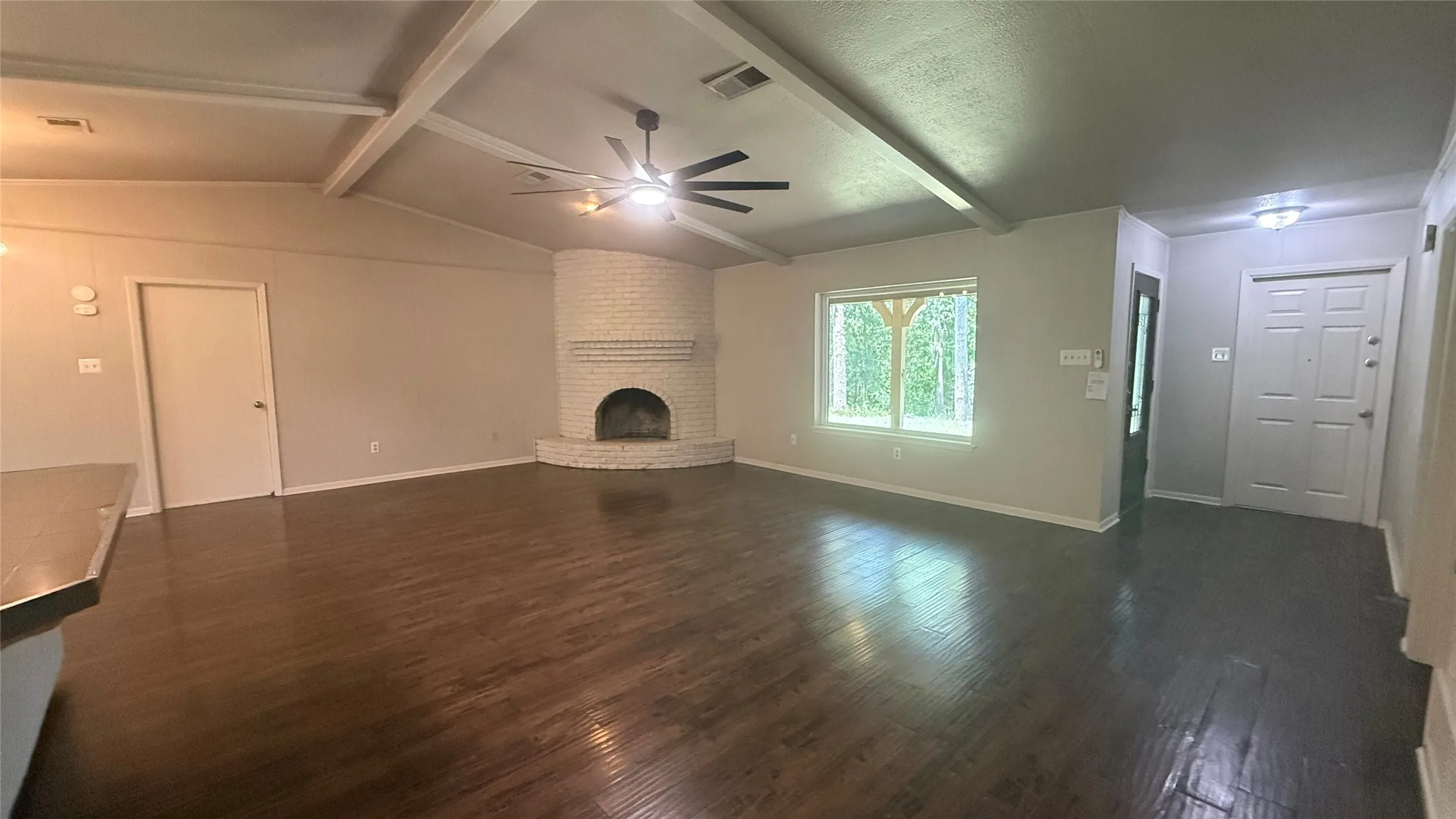 Spacious living area featuring wood-finish flooring, an exposed beam ceiling, and a corner brick fireplace