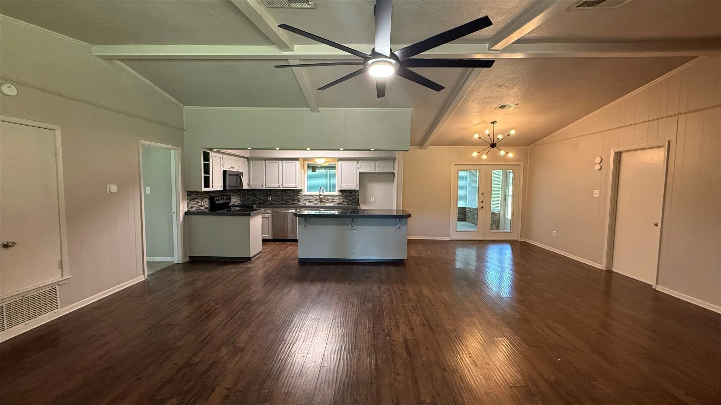 Open-concept living area featuring wood-finish flooring, a vaulted ceiling with exposed beams, and a modern ceiling fan