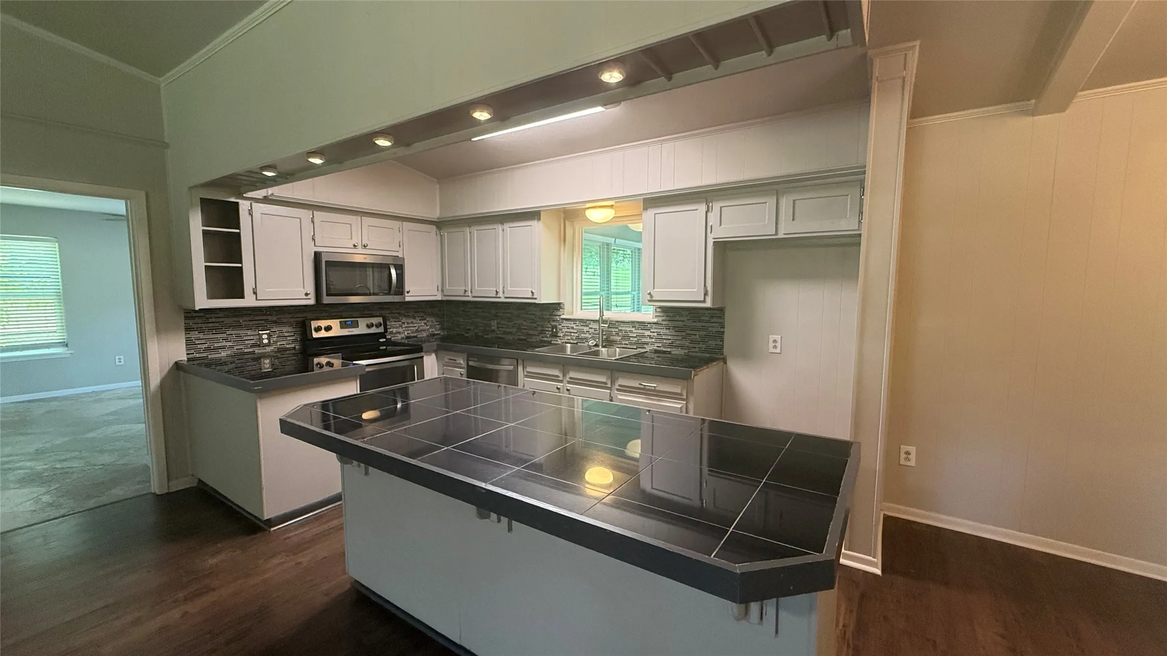 Kitchen featuring light-toned cabinetry, stainless steel appliances, dark countertops, and a tile backsplash