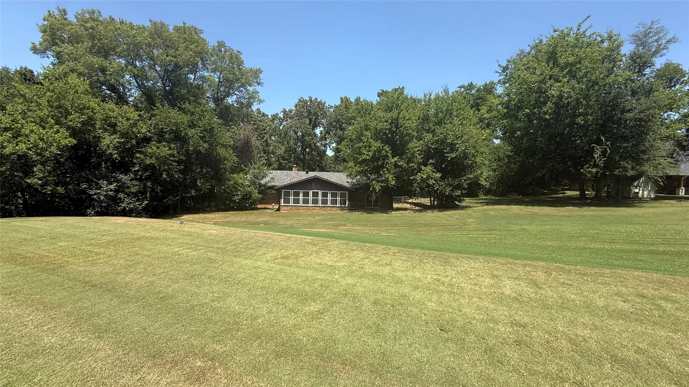 Expansive green lawn bordering a single-story residence with a gabled roof and a wall of windows