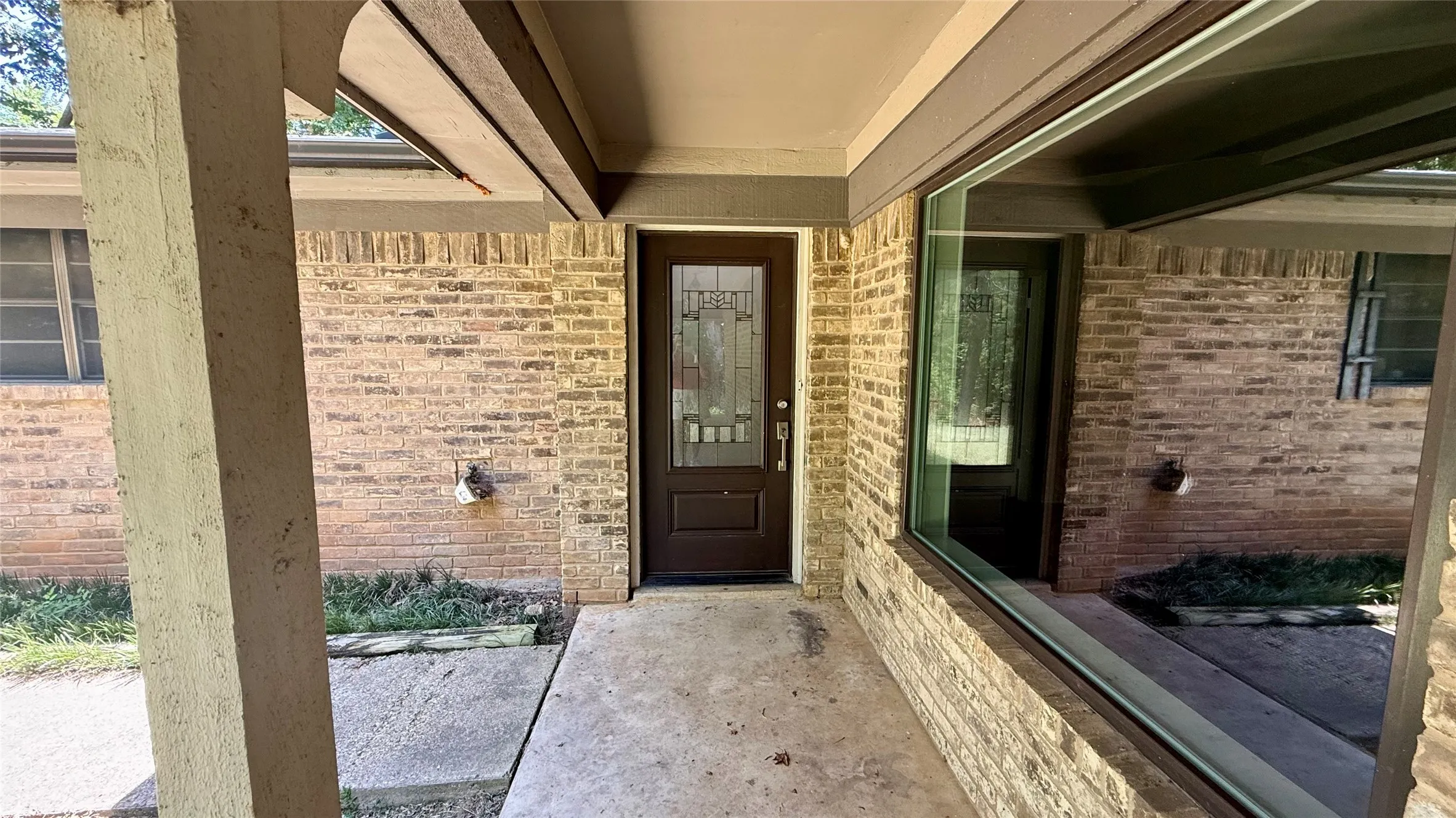 Brick exterior with a covered entry, featuring a decorative glass panel front door and a prominent fixed window