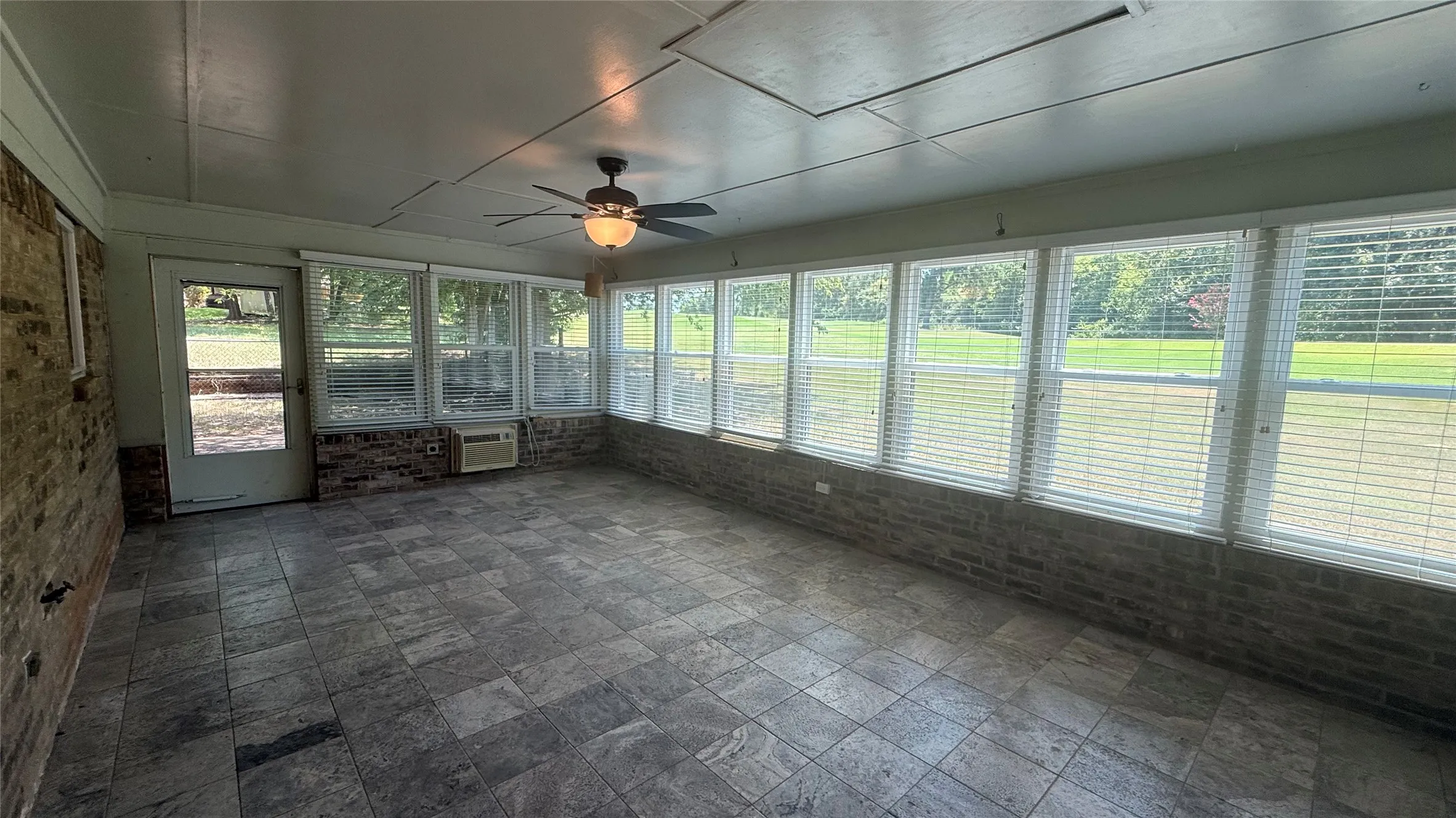 Enclosed sunroom featuring extensive window-lined walls, a tiled floor, a ceiling fan with integrated lighting, and a brick half-wall